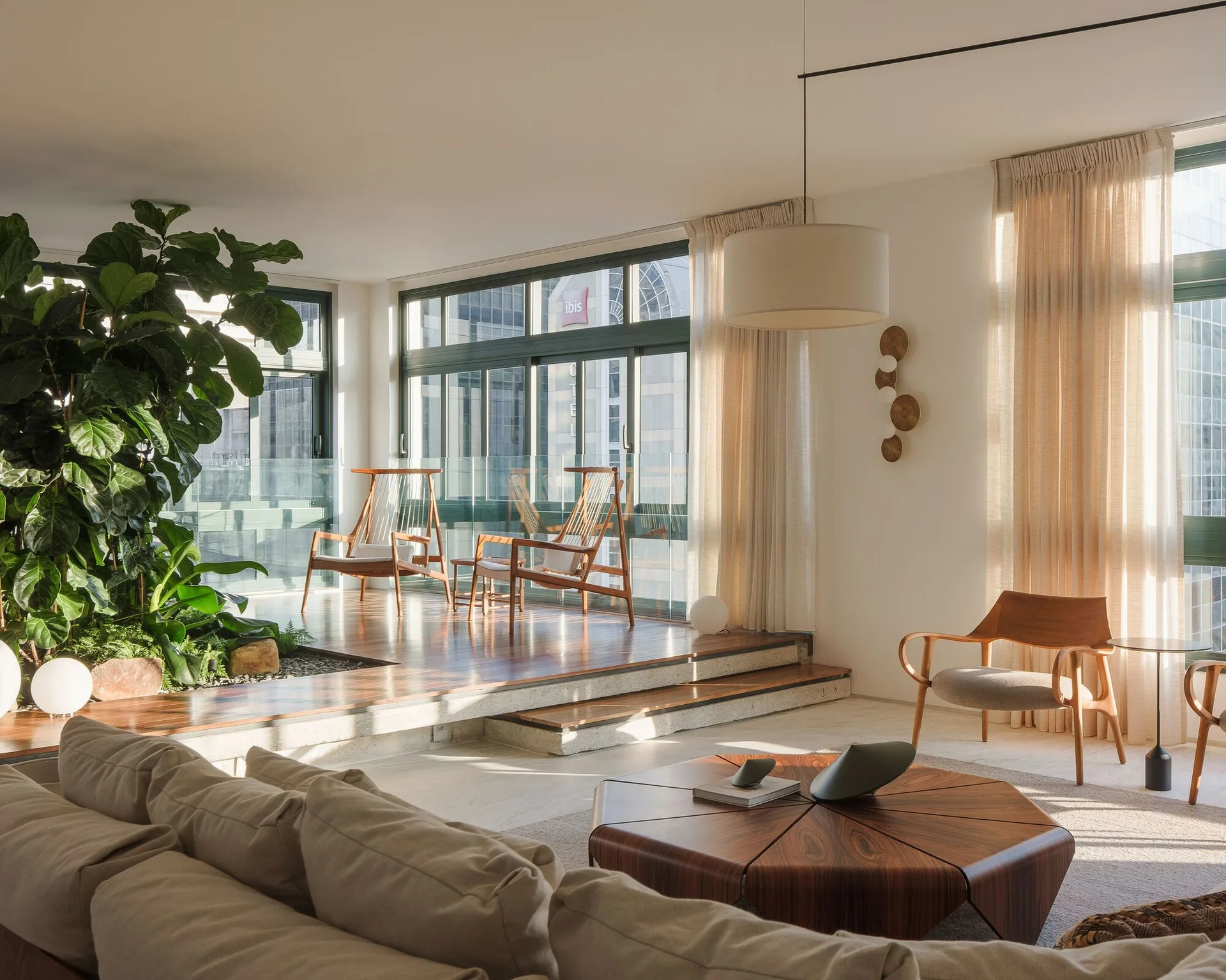 A modern living room featuring a raised wooden platform with lounge chairs, a sunken lounge area with a sofa, and an integrated indoor garden.