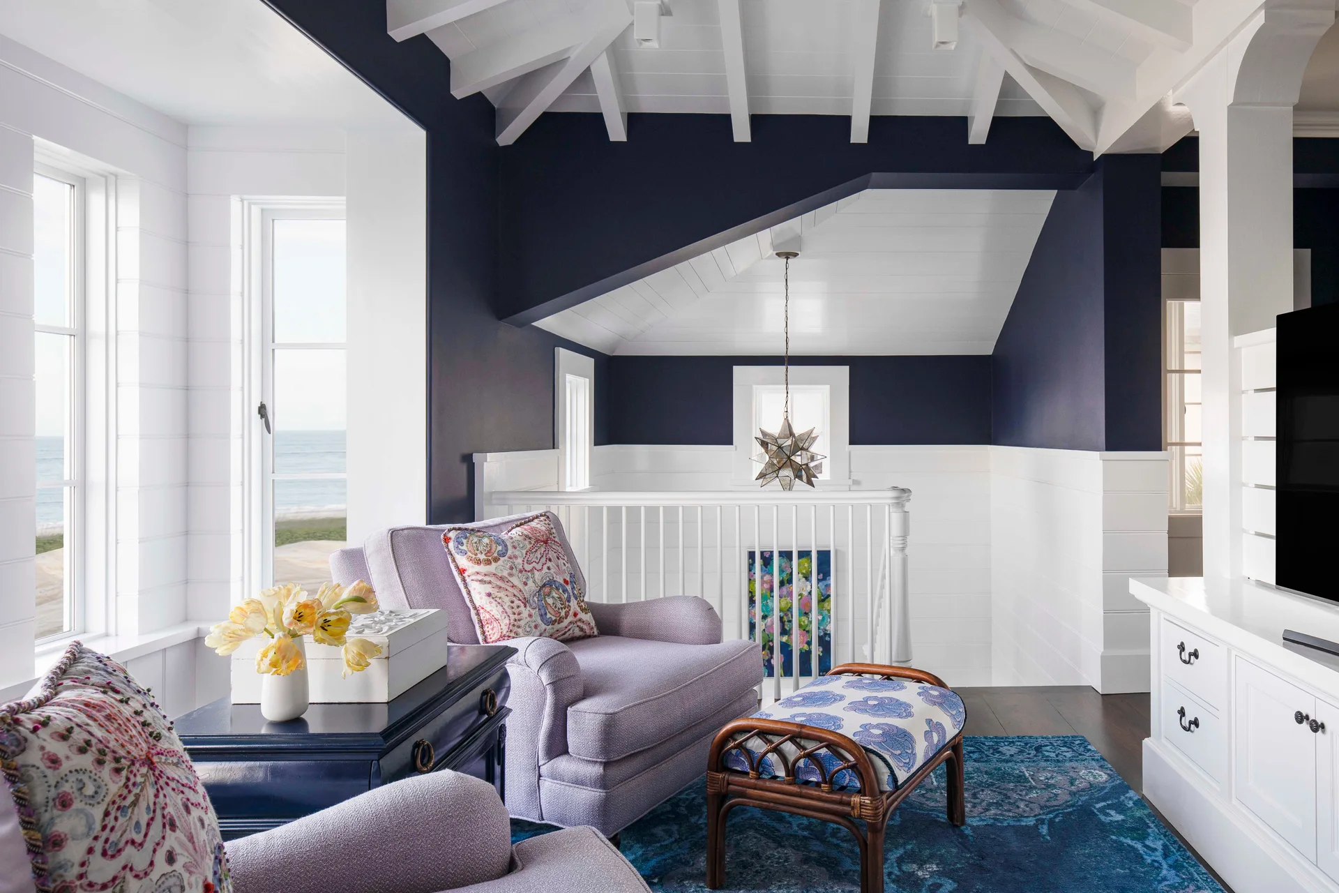 A coastal landing sitting area with lavender armchairs, a patterned blue rug, white shiplap walls, and a deep navy painted ceiling vault.