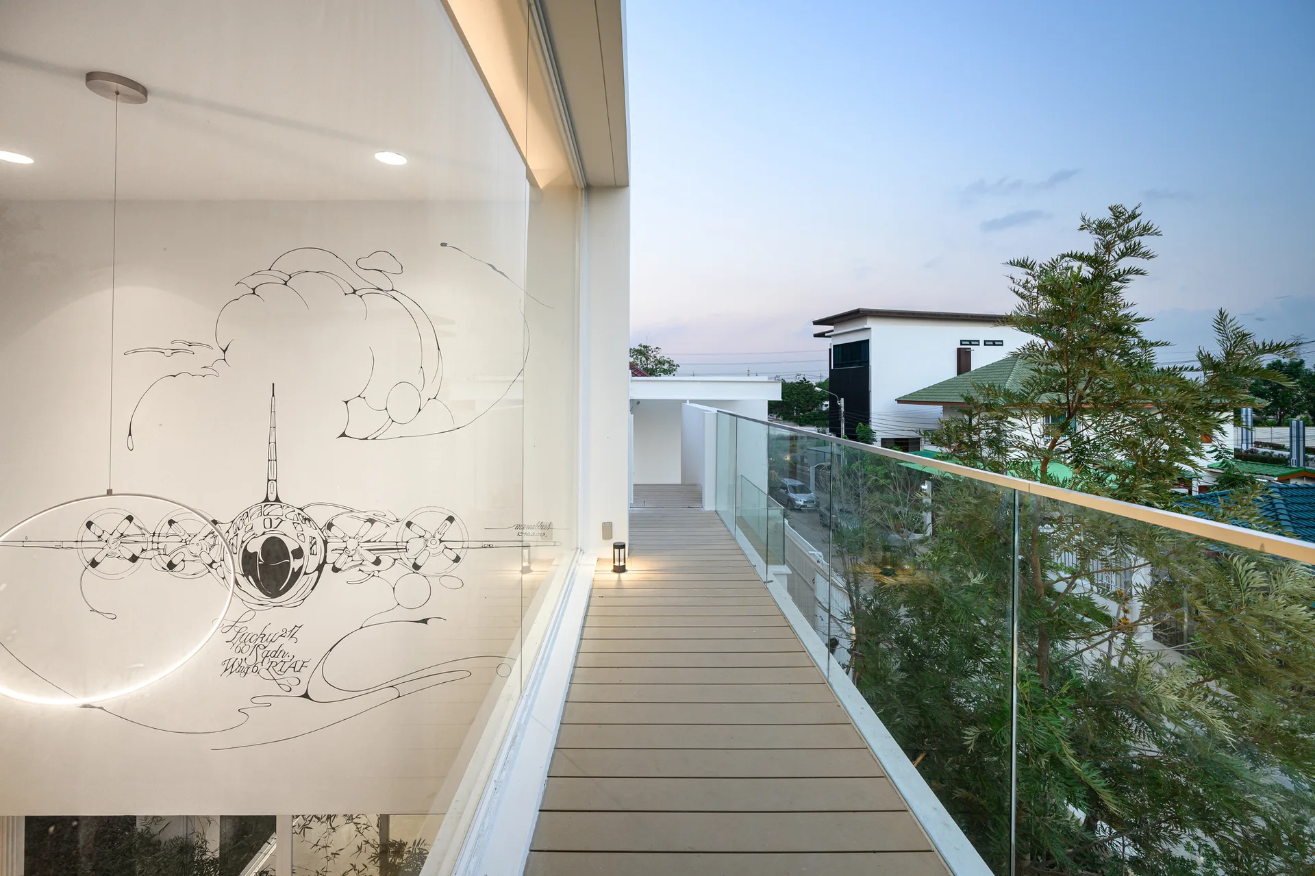 A minimalist balcony features wood-look plank decking, a frameless glass railing, and a large window showcasing a line-drawn airplane illustration.