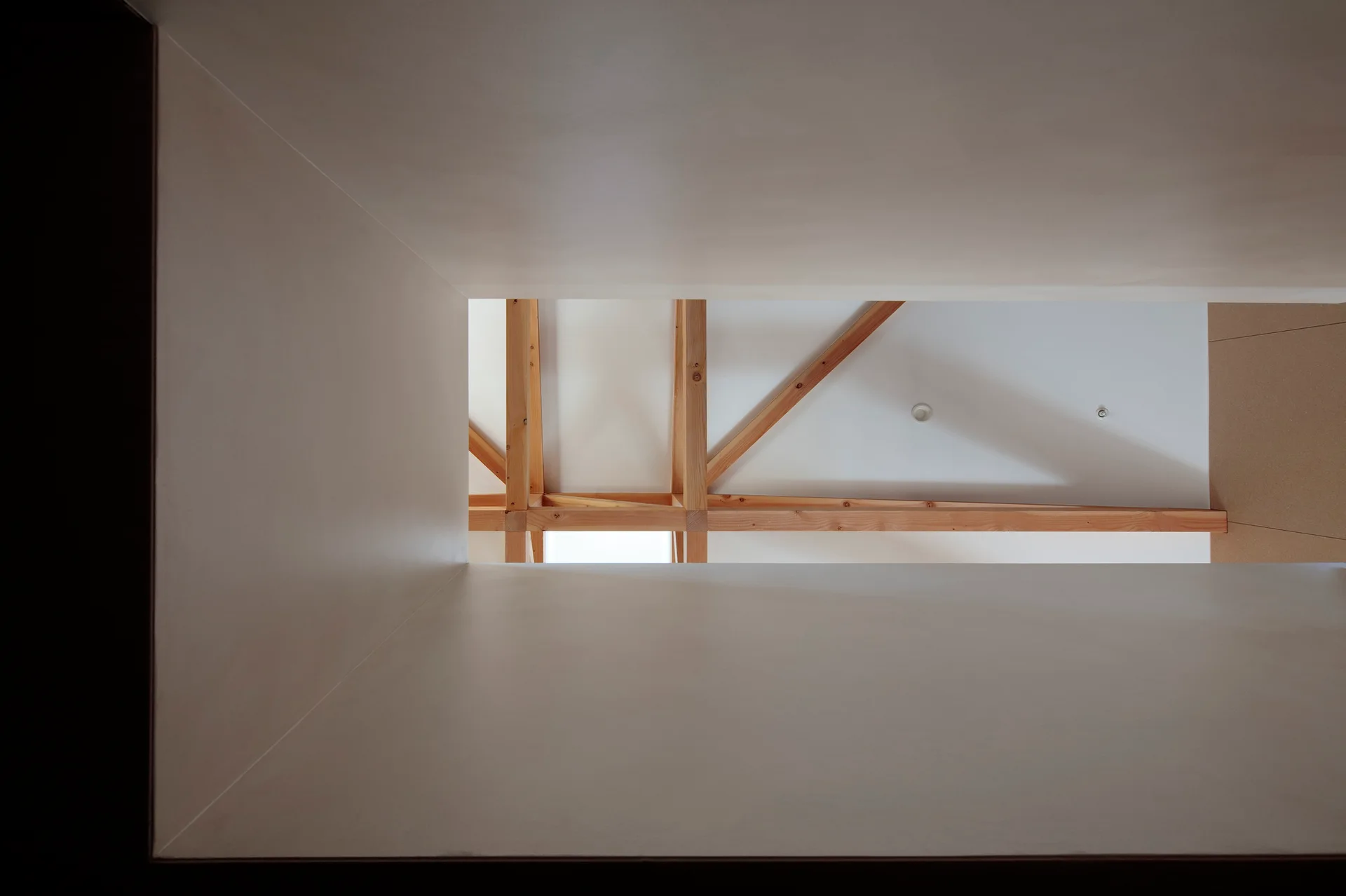 A view looking up through a clean white rectangular opening at a flat ceiling featuring exposed light wood trusses.