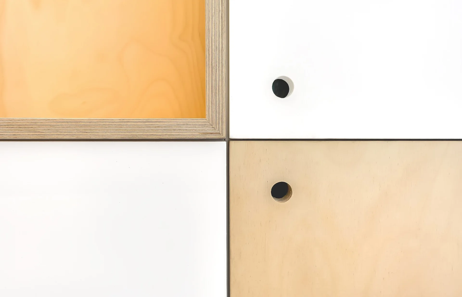 Close-up of modular cabinet doors showing a grid of alternating matte white laminate and light plywood panels with round finger pull cutouts.
