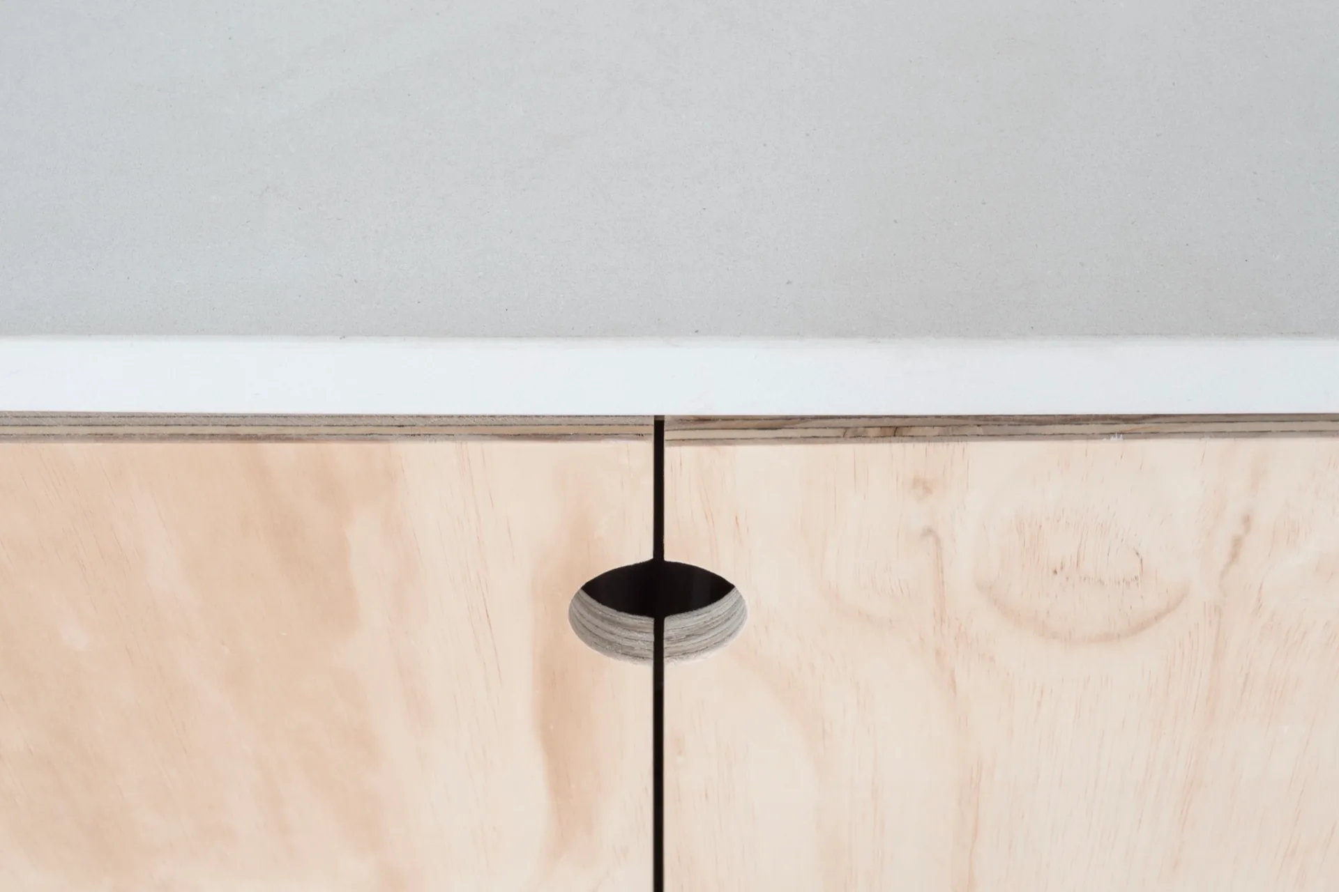 Close-up of a light gray countertop above flat-front plywood cabinets featuring a circular cutout handle.