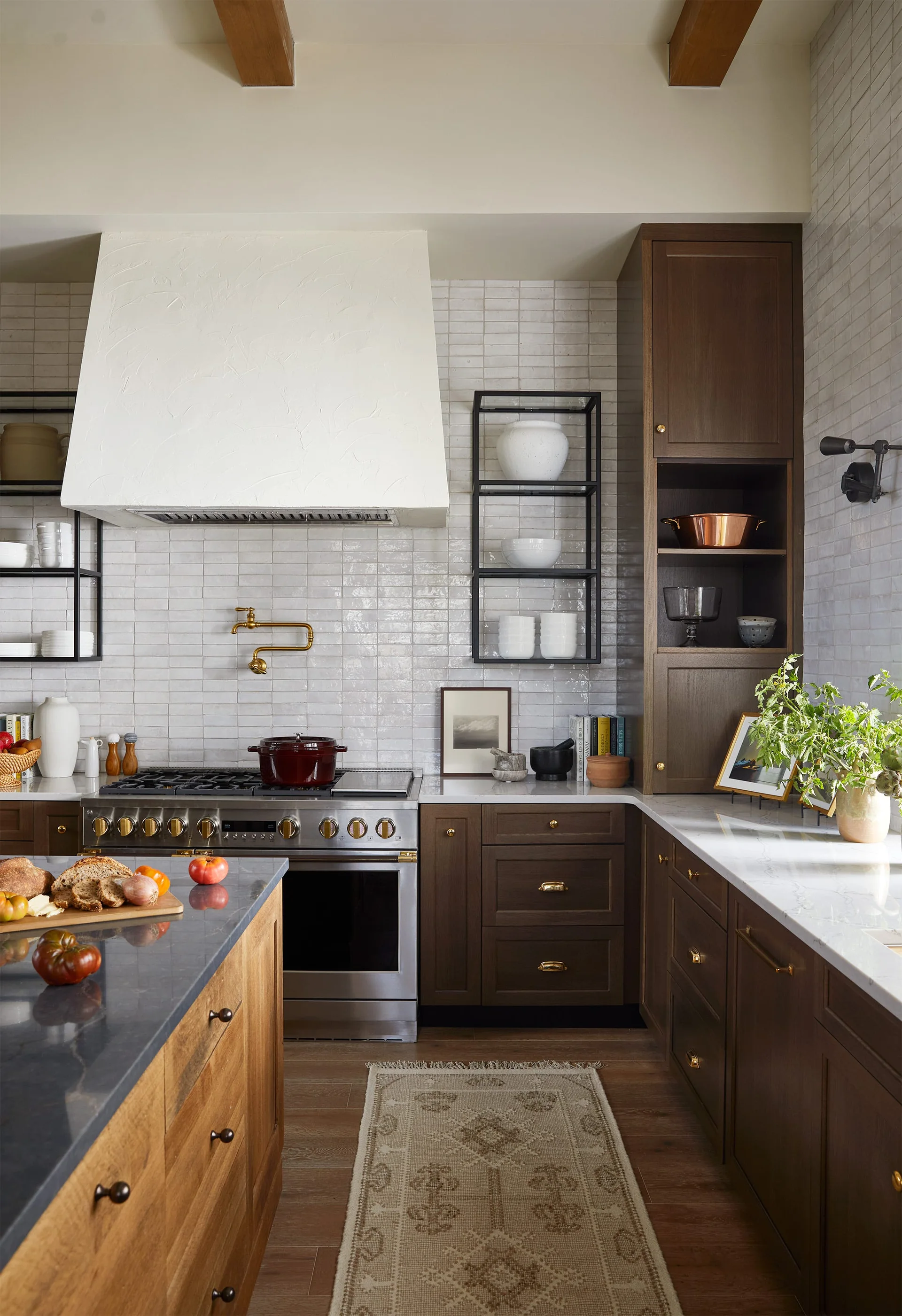 A kitchen features dark wood cabinets, a textured white tile backsplash, a plaster range hood, and a stainless steel range with a brass pot filler.