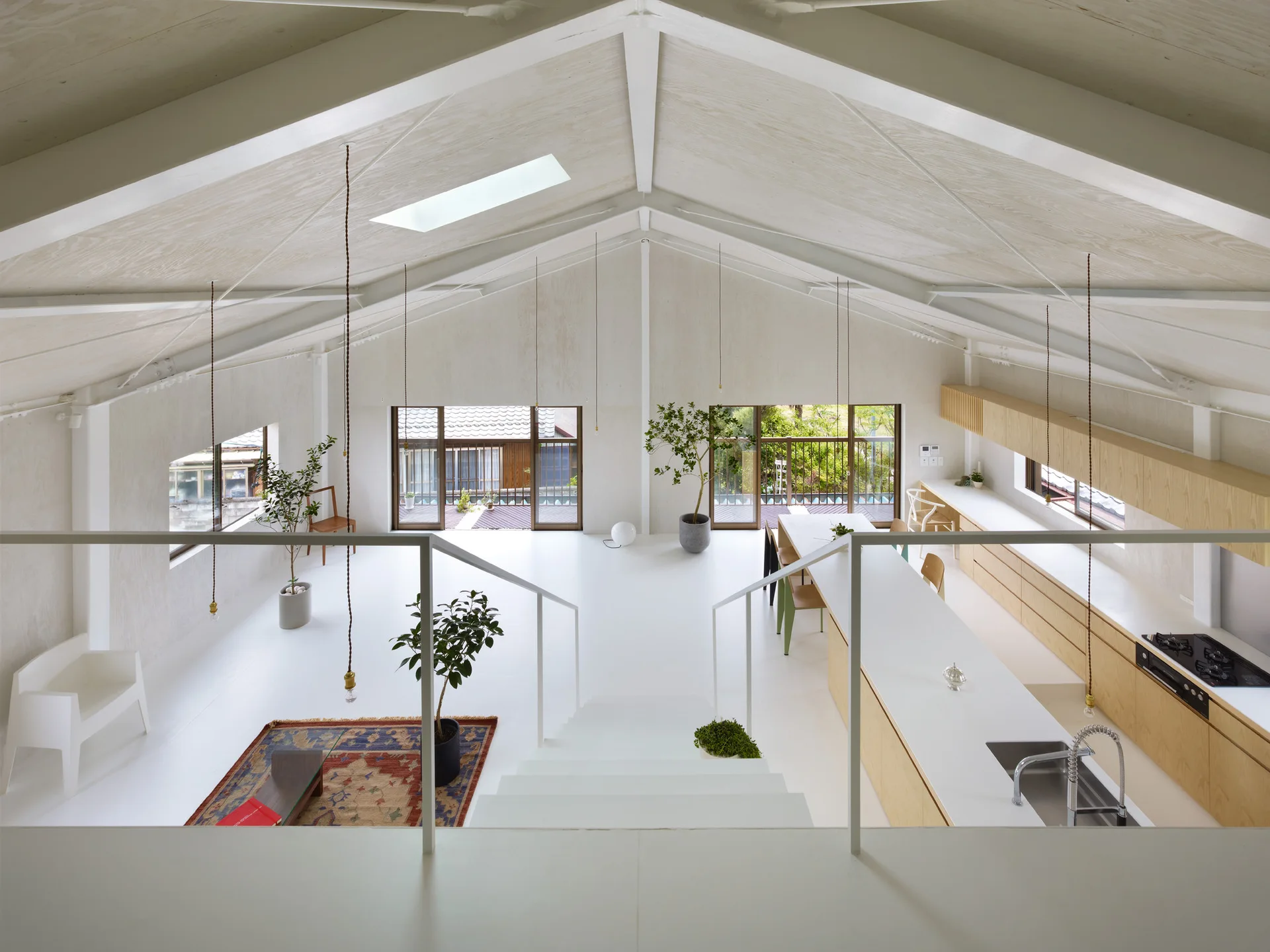 Elevated view of an open-plan living and kitchen space with a vaulted wood ceiling, white floors, and light wood cabinetry.