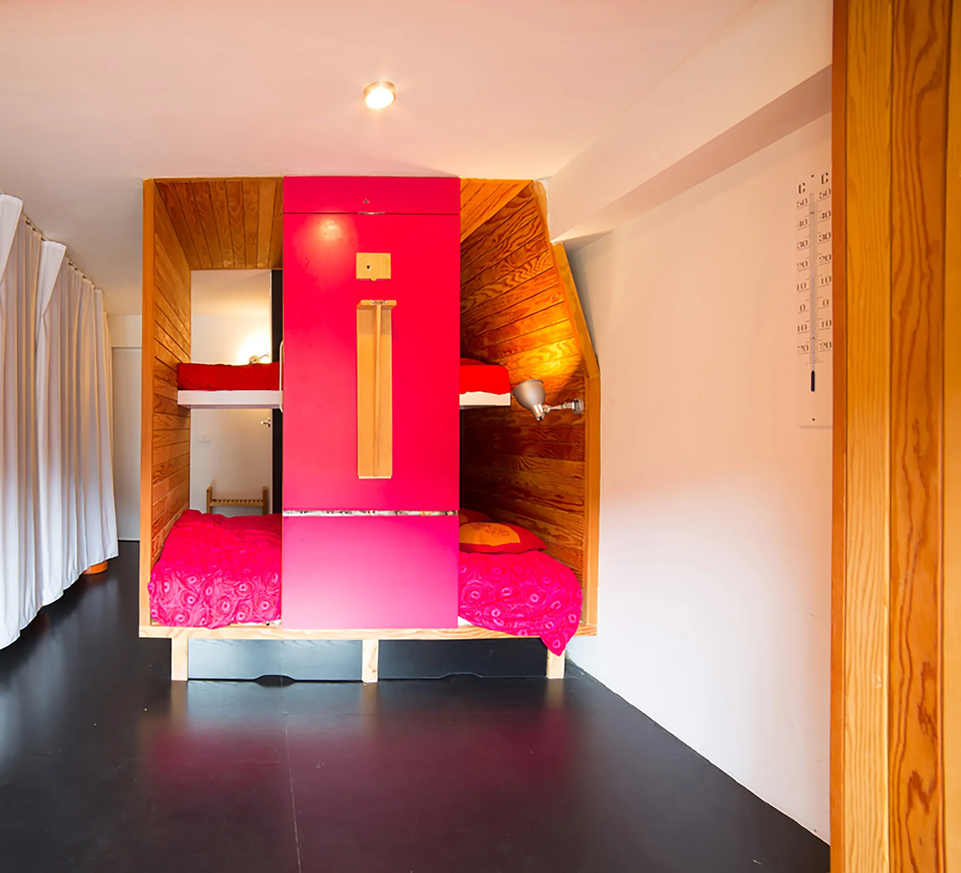 Built-in bunk beds lined with natural wood paneling are separated by a bright pink central cabinet on a dark floor.