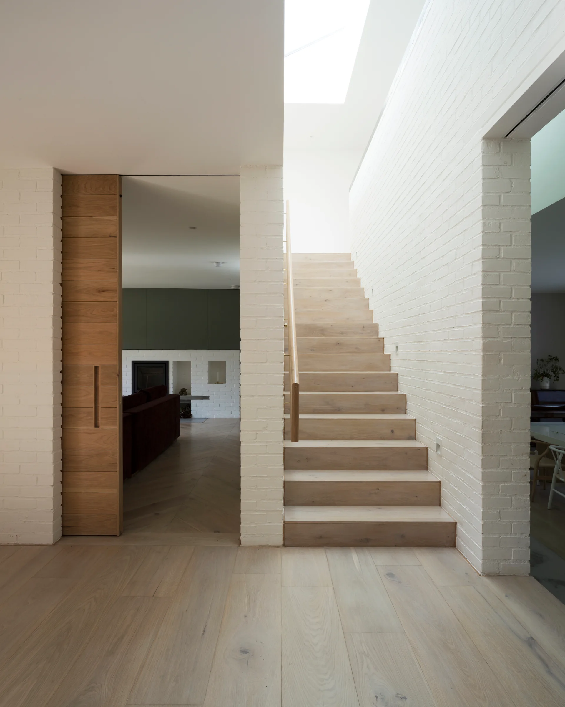 A light wood staircase ascends between white painted brick walls next to a tall wooden sliding pocket door and light oak floors.