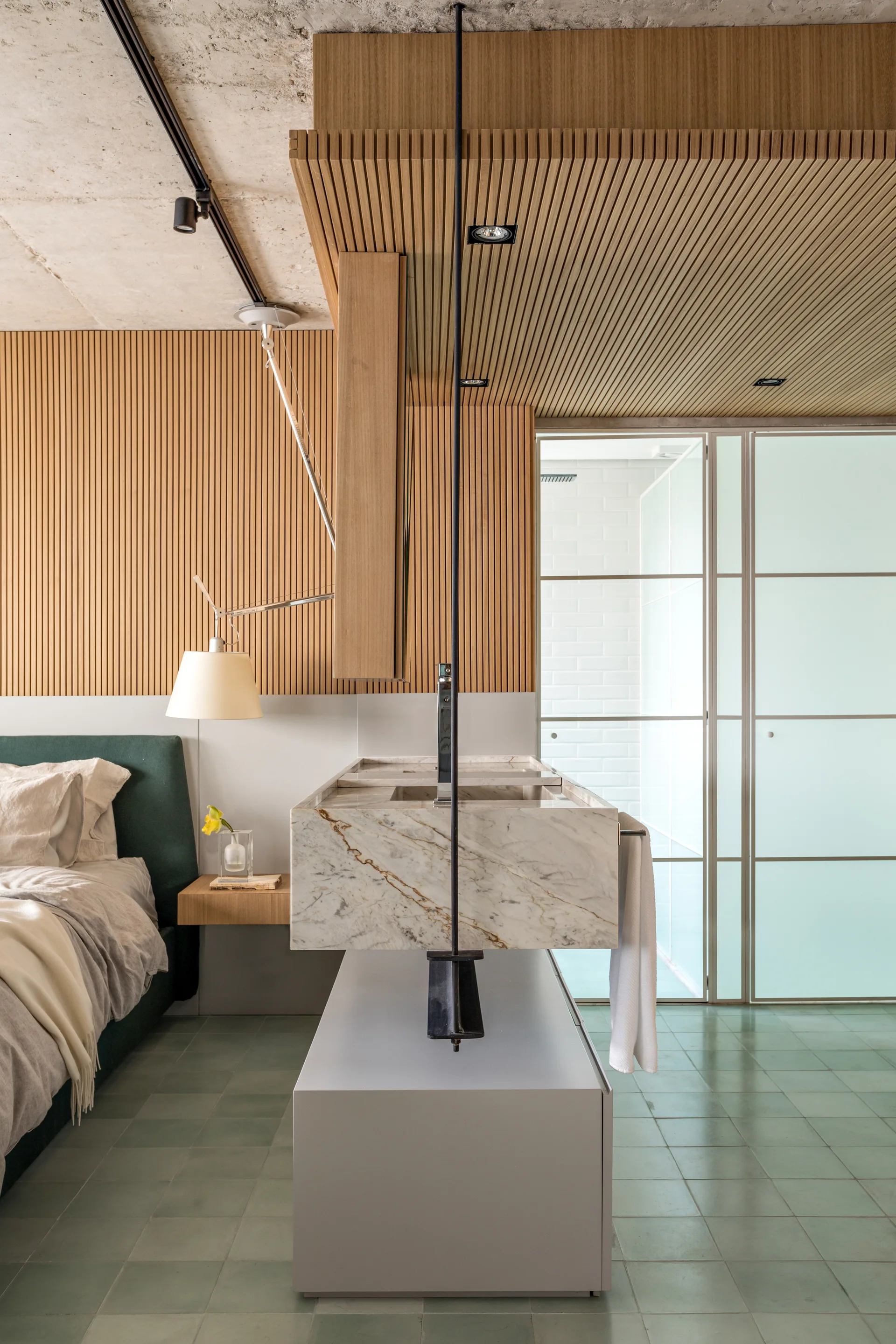 A contemporary bedroom ensuite features a green headboard bed, a freestanding marble vanity, and vertical slatted wood wall paneling.