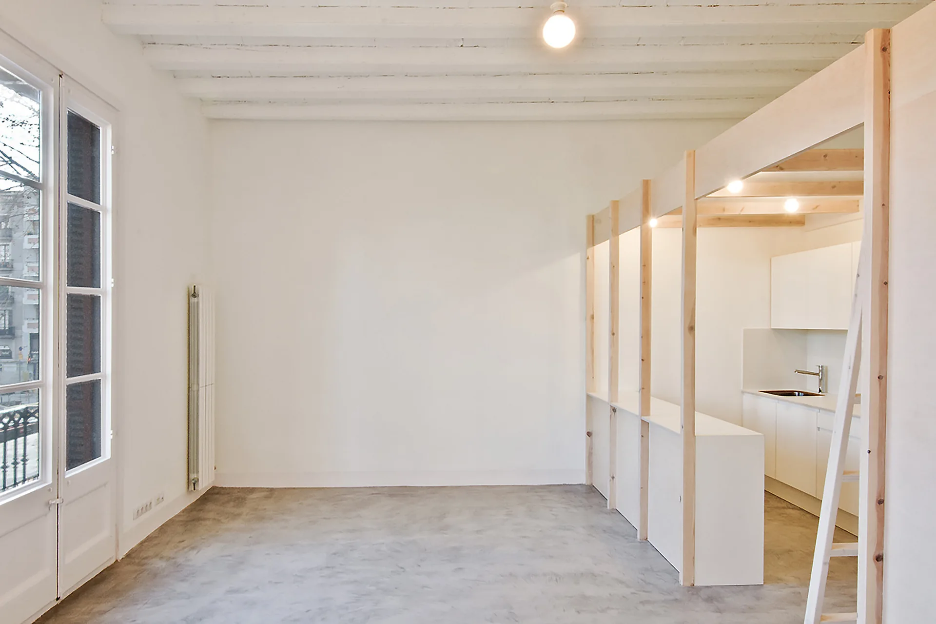 A minimalist interior with concrete floors, white walls, and a kitchenette built into a custom light wood timber frame.