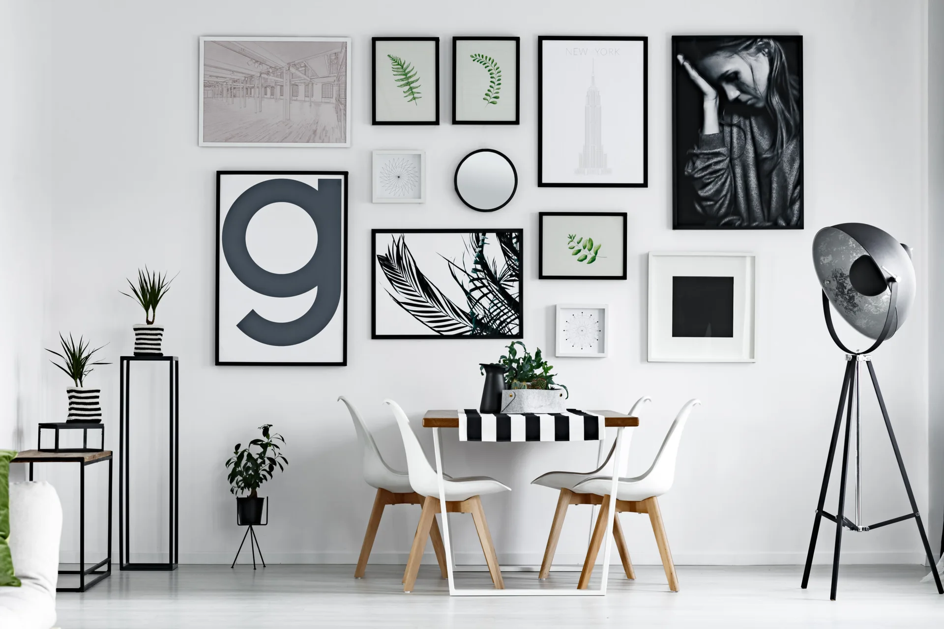 A minimalist dining table and white molded chairs are set against a large black and white gallery wall featuring framed graphic art.