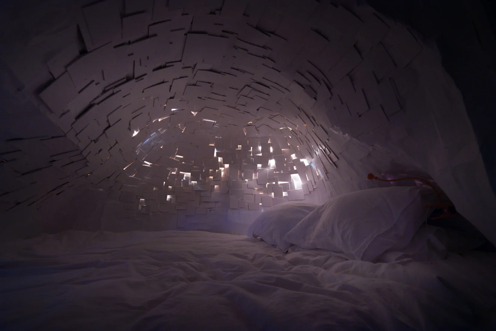 A low-profile bed with white bedding sits under a curved, arched ceiling made of overlapping white panels with integrated backlighting.