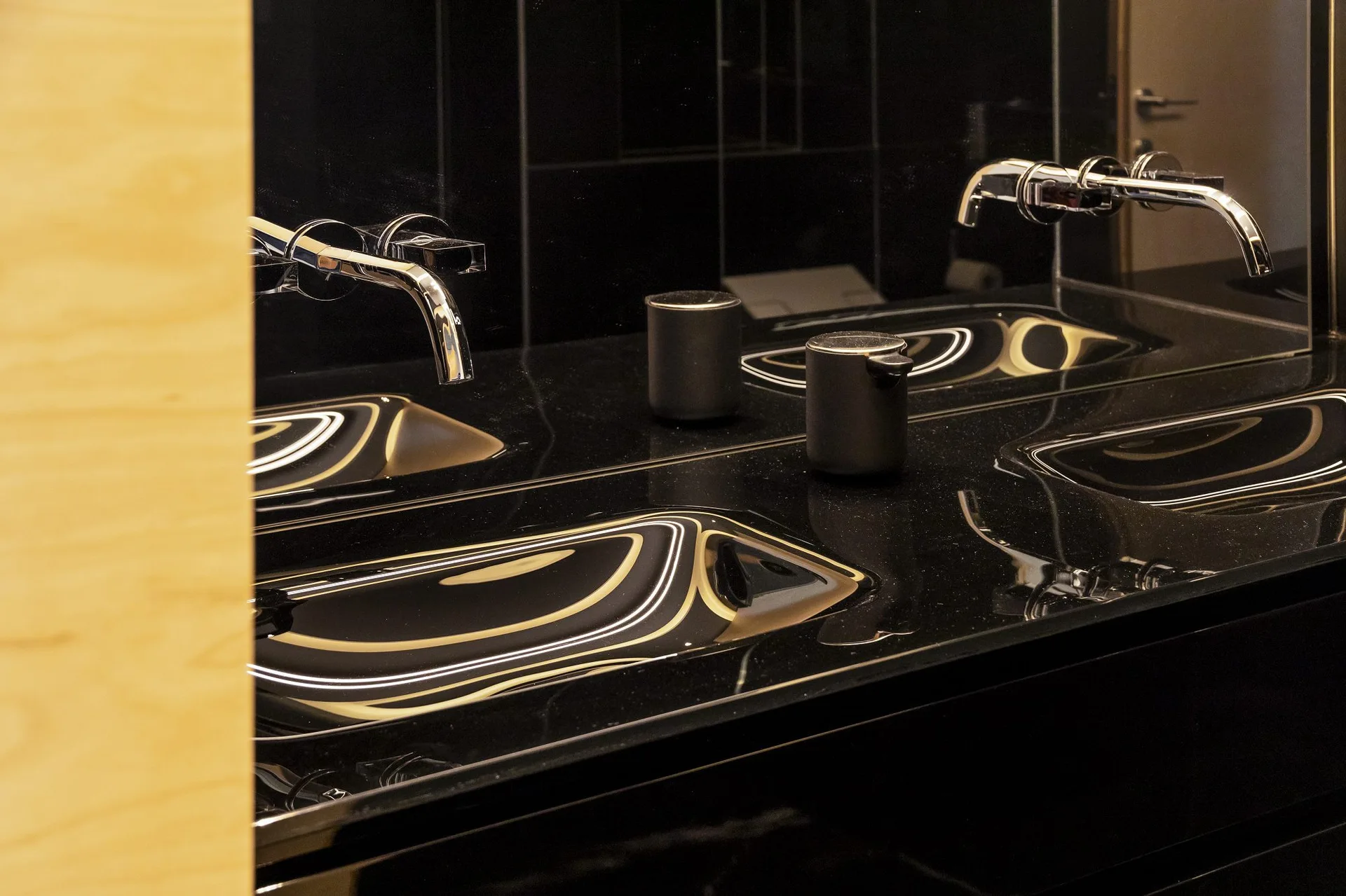 A close-up of a glossy black bathroom vanity featuring an integrated sink, a wall-mounted chrome faucet, and a black soap dispenser.
