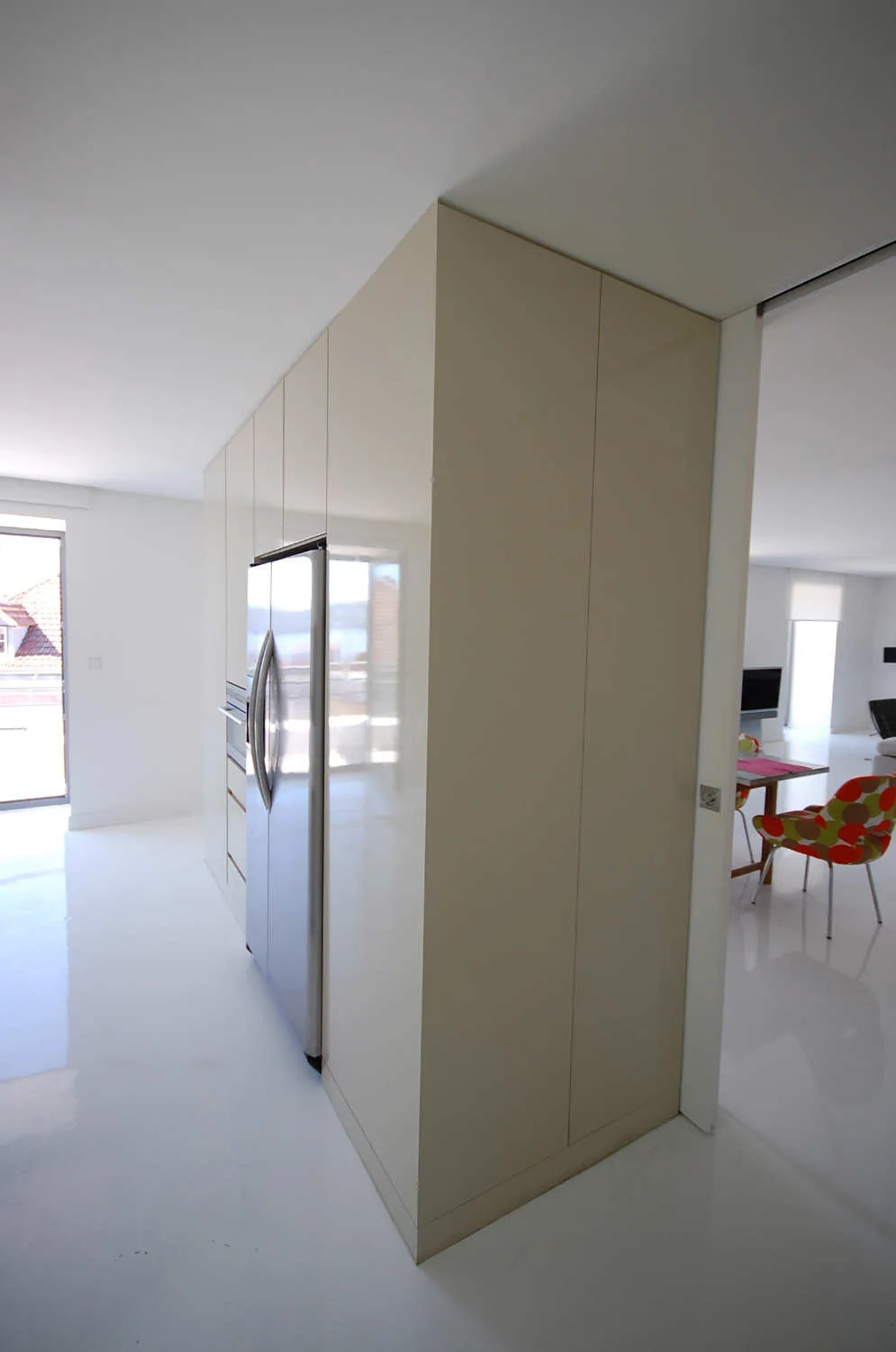 A modern kitchen with tall high-gloss beige cabinetry, a built-in stainless steel refrigerator, and reflective white flooring.