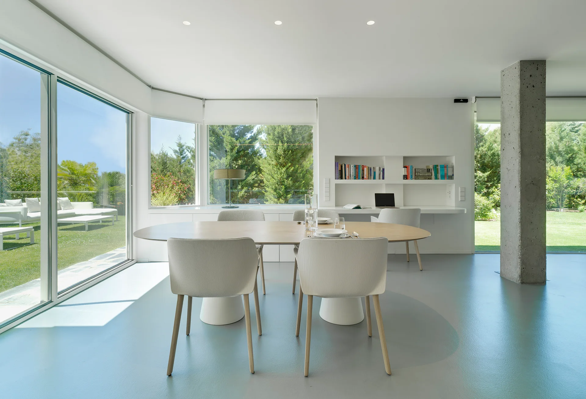 A minimalist dining room features a light wood table, white chairs, a built-in study alcove, and an exposed concrete column.