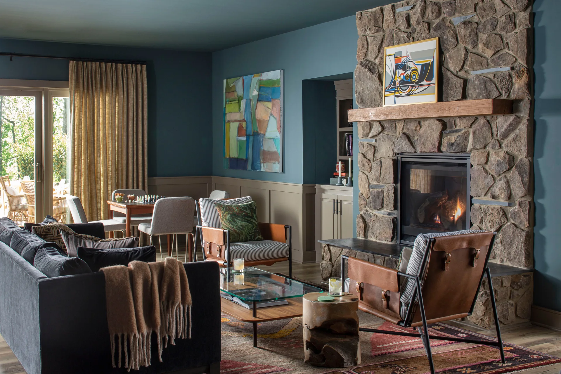 A living room features dark blue walls, a large stone fireplace, leather accent chairs, and a glass coffee table over a patterned rug.