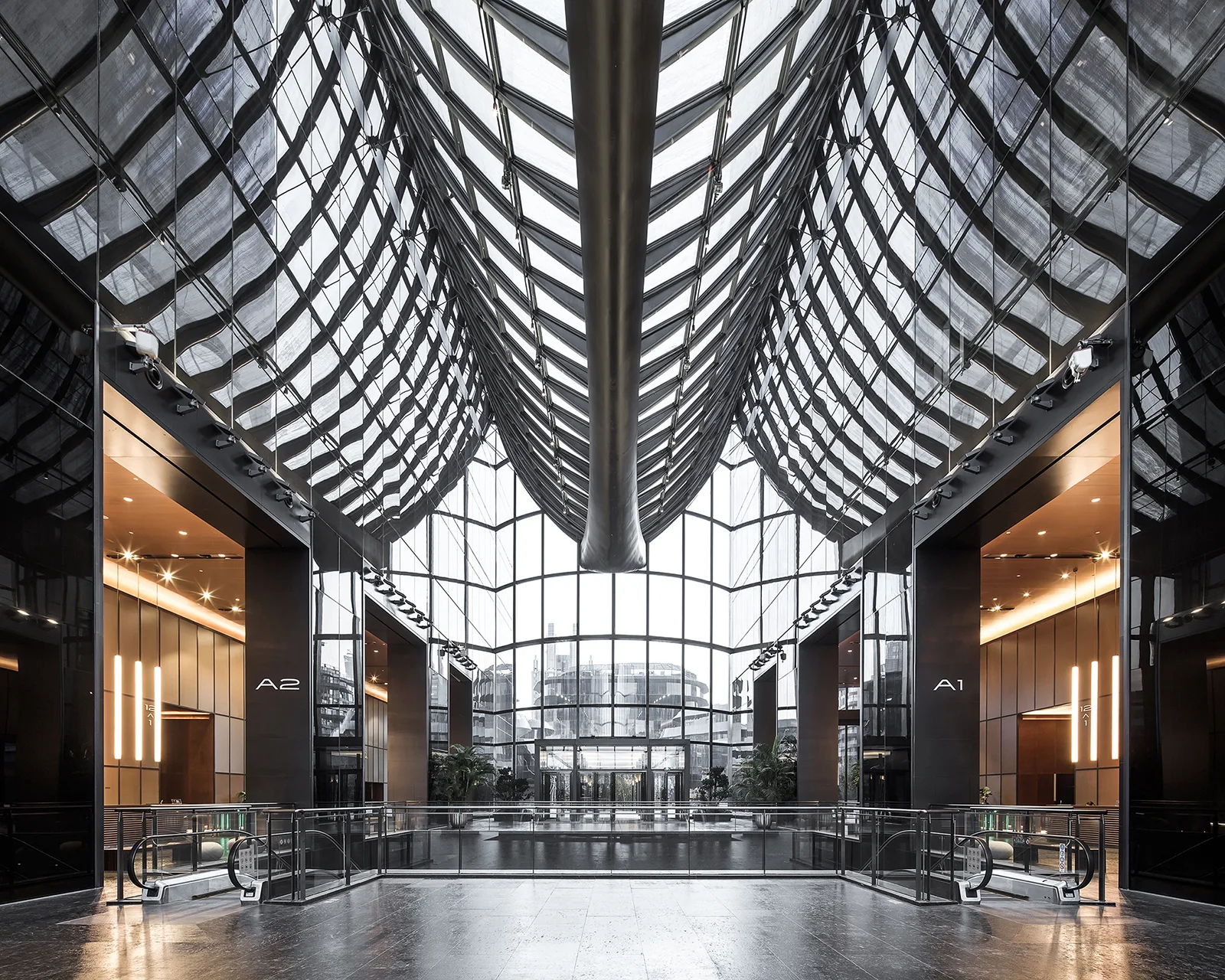 A symmetrical commercial lobby features a high arched glass atrium ceiling, twin escalators, and polished dark flooring.