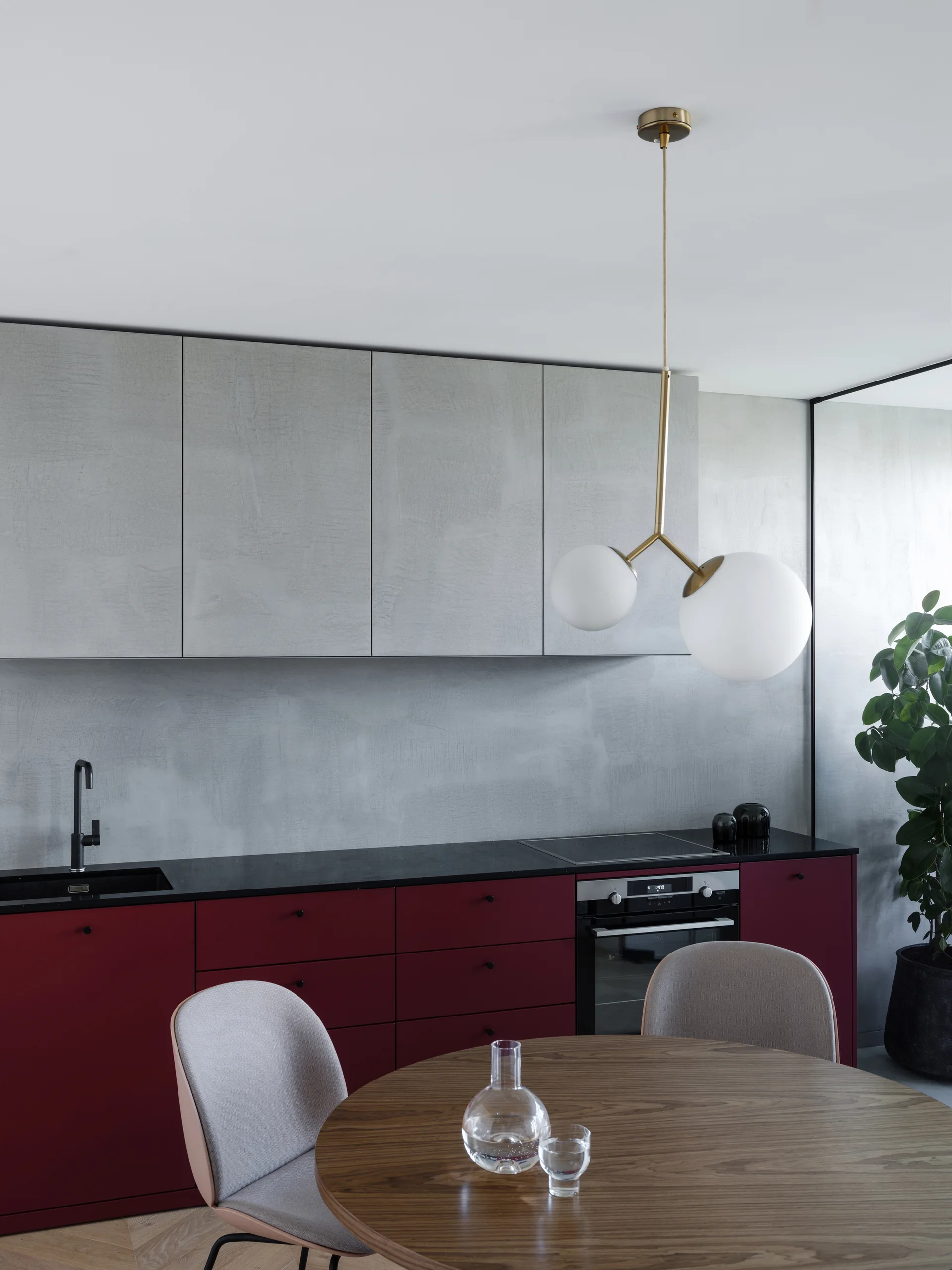 A modern minimalist kitchen features matte burgundy cabinets, textured gray upper cabinets, and a round wood dining table with gray chairs.