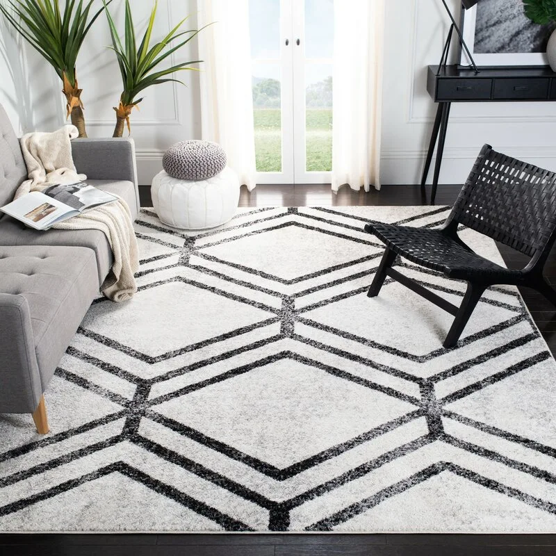 A modern living room features a large white area rug with a black geometric diamond pattern, alongside a grey sofa and black woven leather chair.