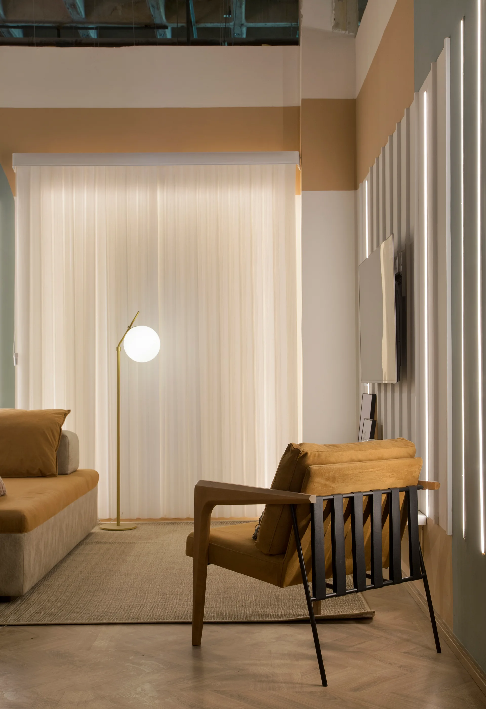 A modern living room features an ochre armchair and sofa, a globe floor lamp, and a white slatted wall panel with integrated vertical LED lighting.