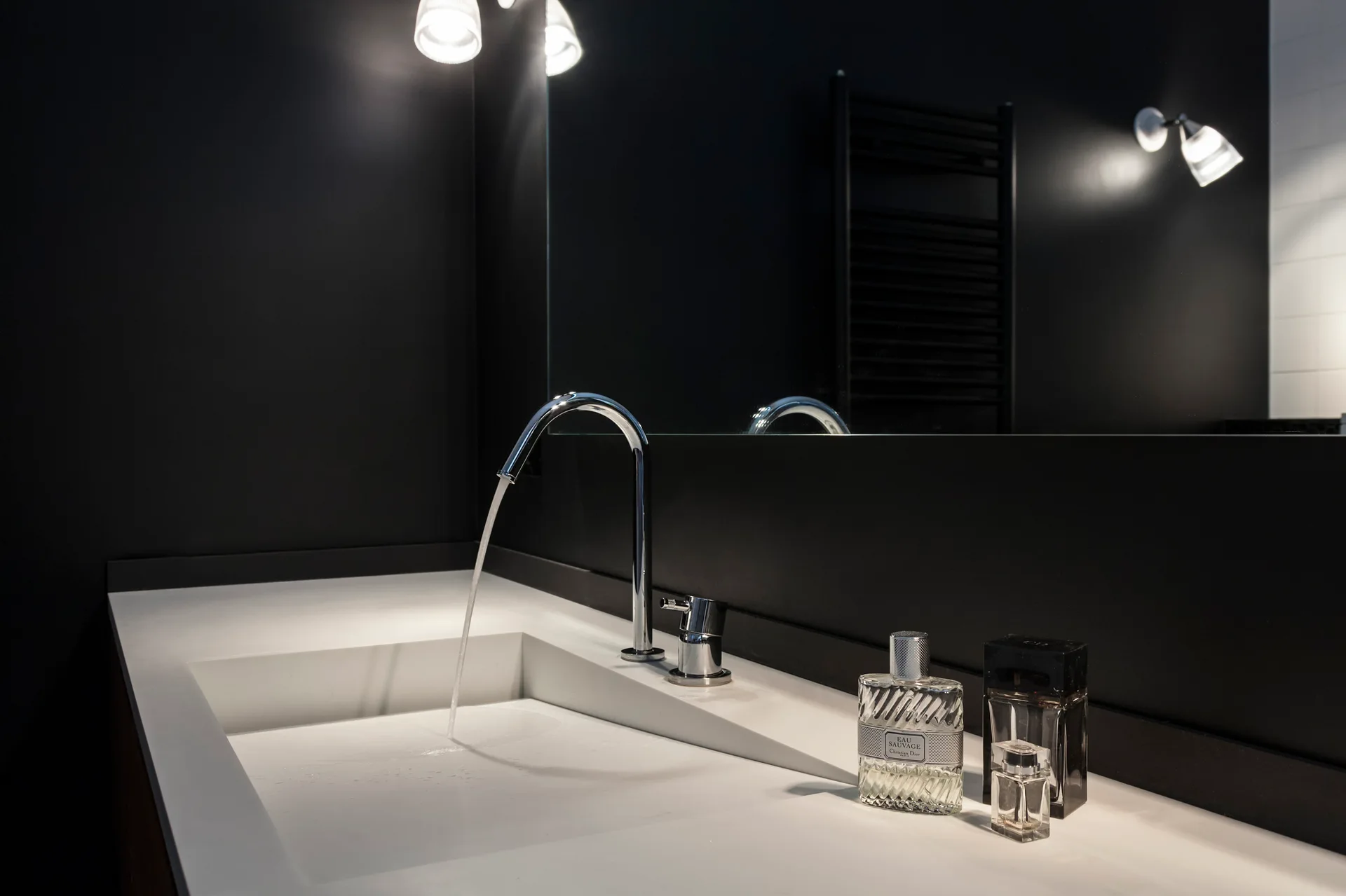 A modern bathroom vanity features an integrated white sink with a curved chrome faucet set against a dark matte wall and a frameless mirror.