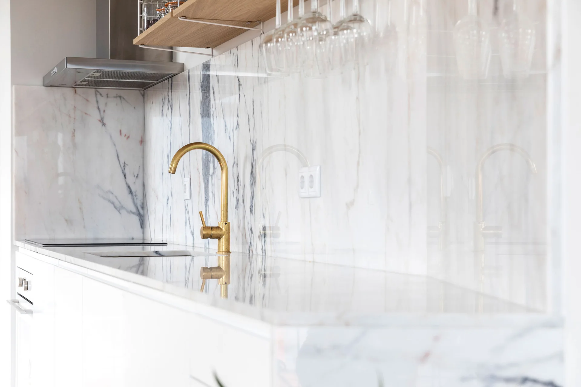 A brushed brass faucet stands on a polished white marble countertop with a matching veined marble slab backsplash.