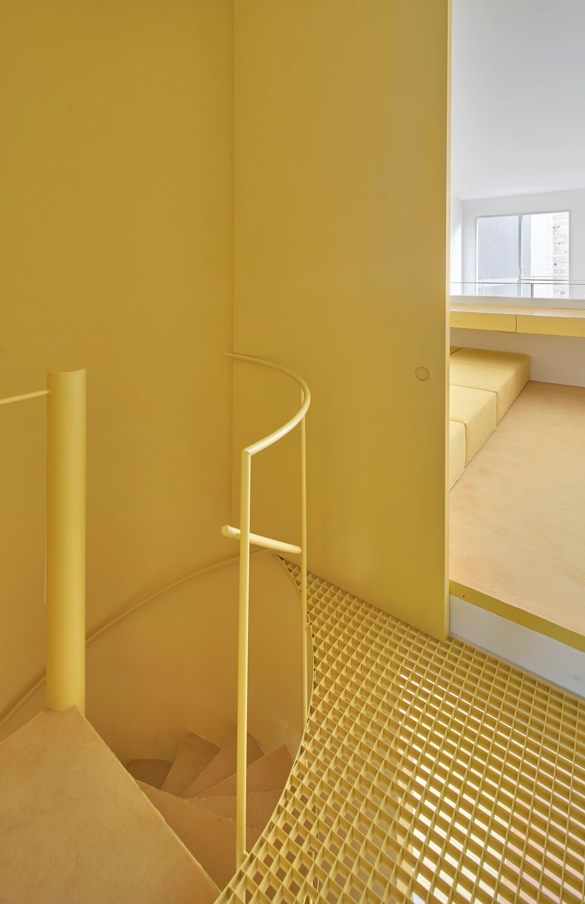 A modern yellow spiral staircase with a metal grate landing leads to an elevated room with built-in seating.