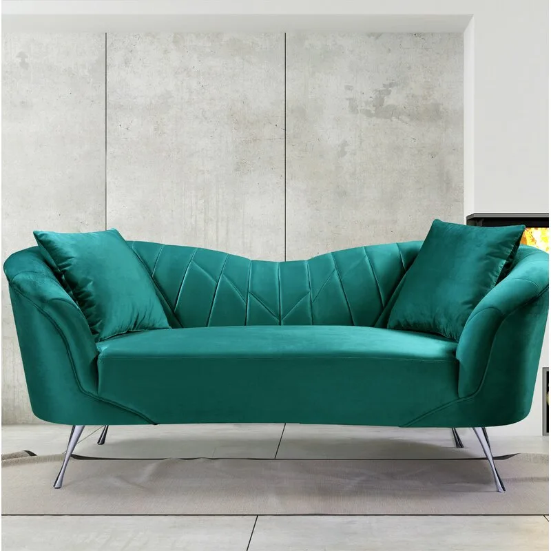 A curved teal velvet sofa with geometric tufting and metallic legs sits in front of a concrete-paneled wall.