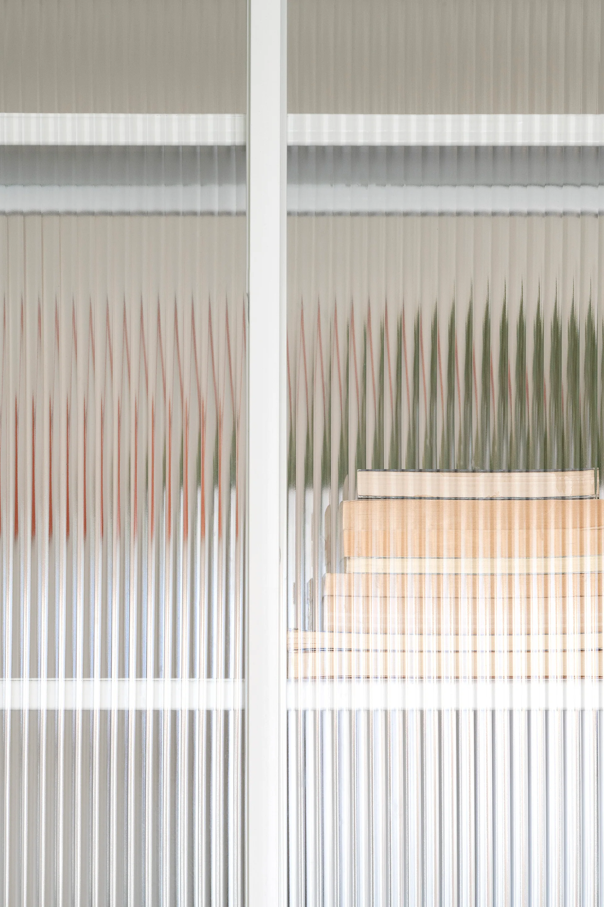 A white cabinet door with vertical fluted glass partially obscuring a stack of books inside.