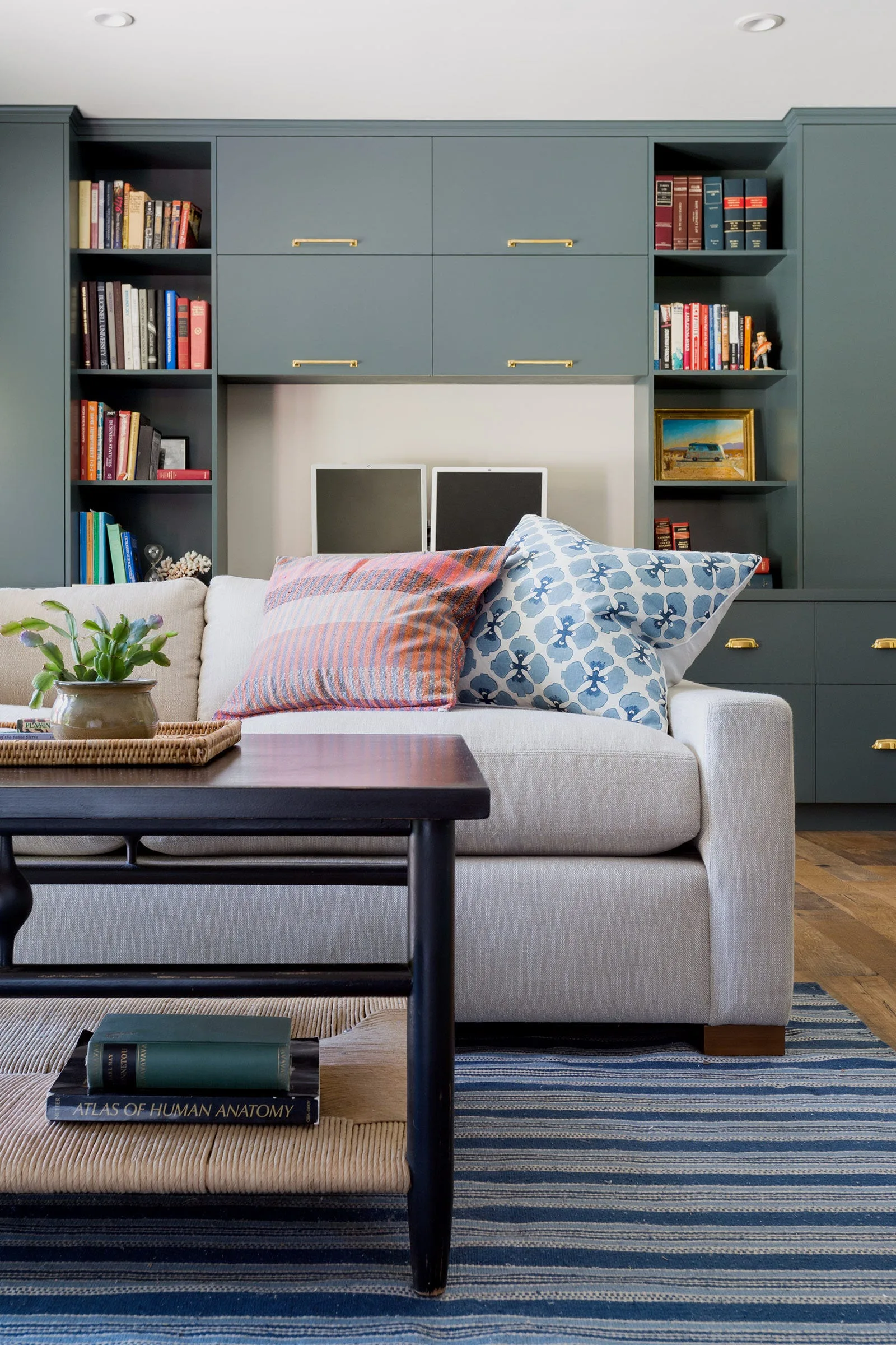 An off-white sofa with patterned pillows sits in front of a deep blue-grey built-in shelving unit and a dark wood coffee table.