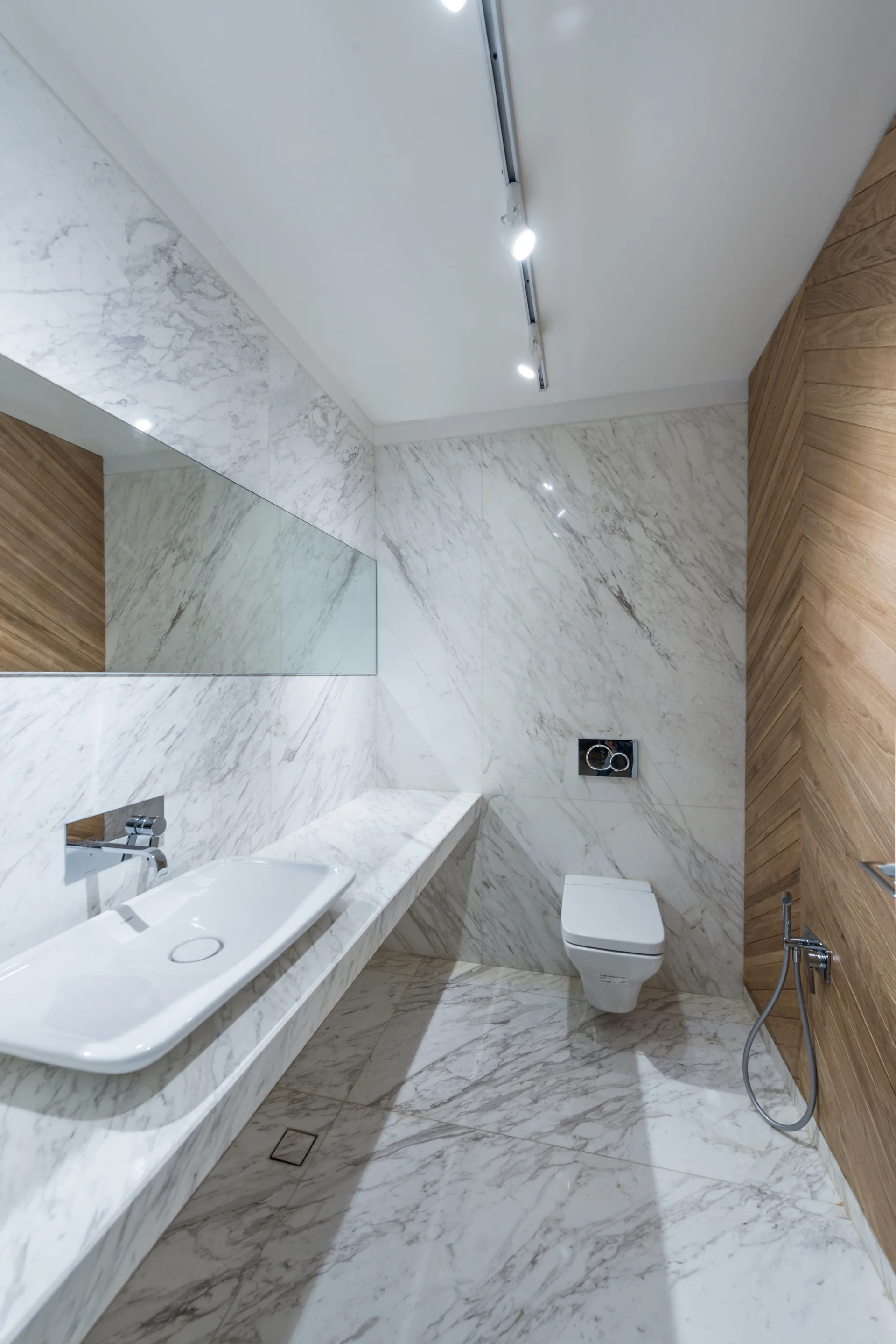 A modern bathroom features white marble slab walls and flooring, a floating marble counter with a white sink, and a chevron wood paneled wall.
