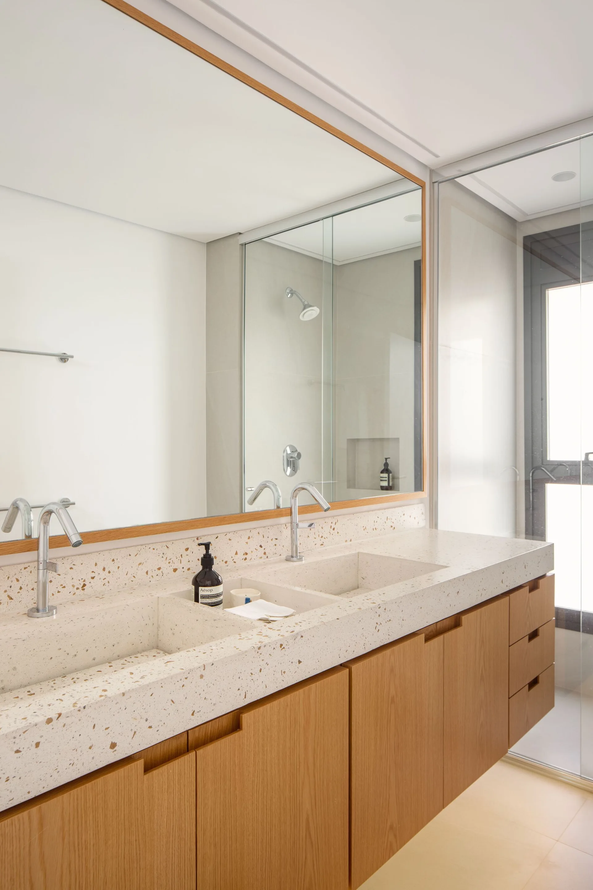 A modern bathroom features a floating light wood vanity with a speckled terrazzo double sink and a matching large wood-framed mirror.