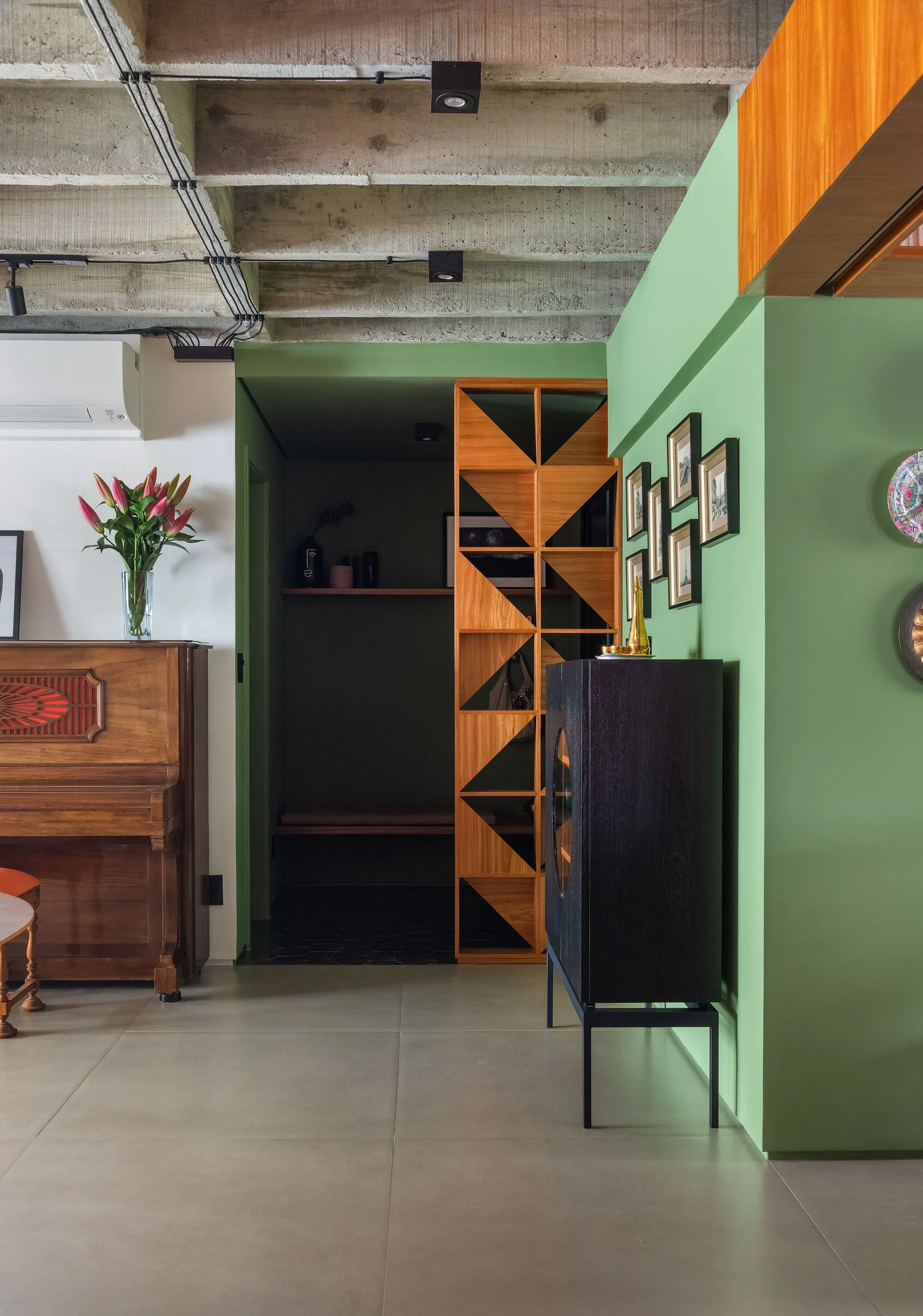 A living room features a green partition wall, an upright wooden piano, a black cabinet, and an exposed concrete ceiling.