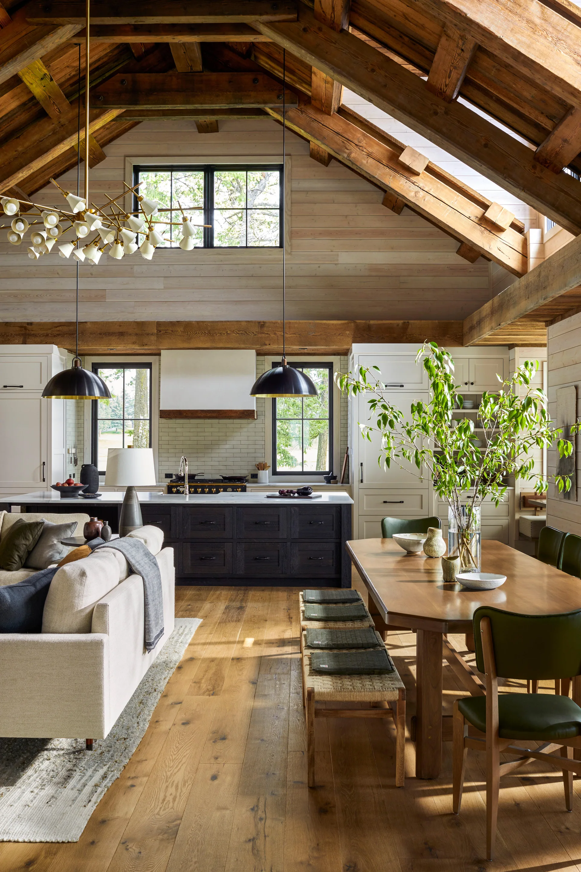 A spacious open-plan kitchen and dining area featuring a vaulted timber ceiling, dark wood kitchen island, and a long wooden dining table.