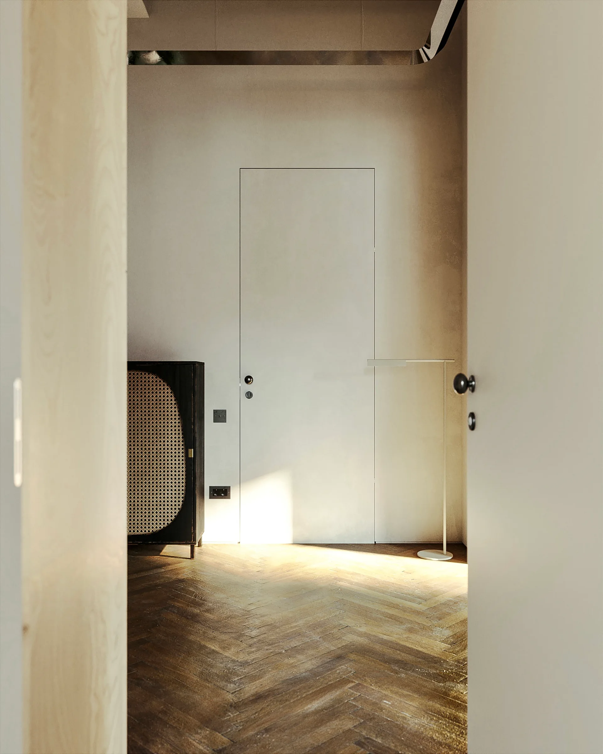 A minimalist hallway features a flush door, a dark cane cabinet, a slim floor lamp, and herringbone pattern wood flooring.