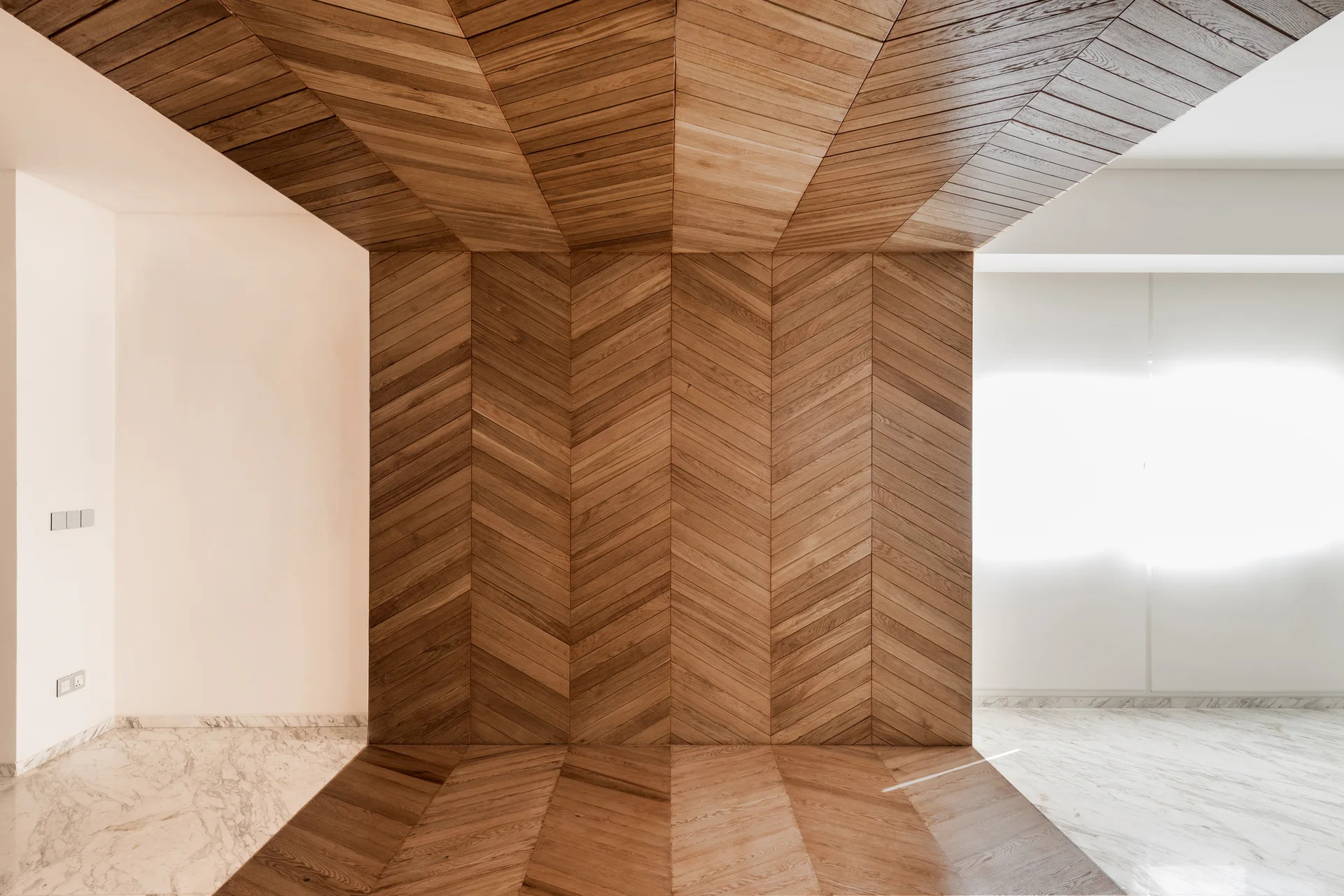 A minimalist room featuring warm chevron wood paneling that extends continuously from the floor up the wall and across the ceiling next to marble flooring.
