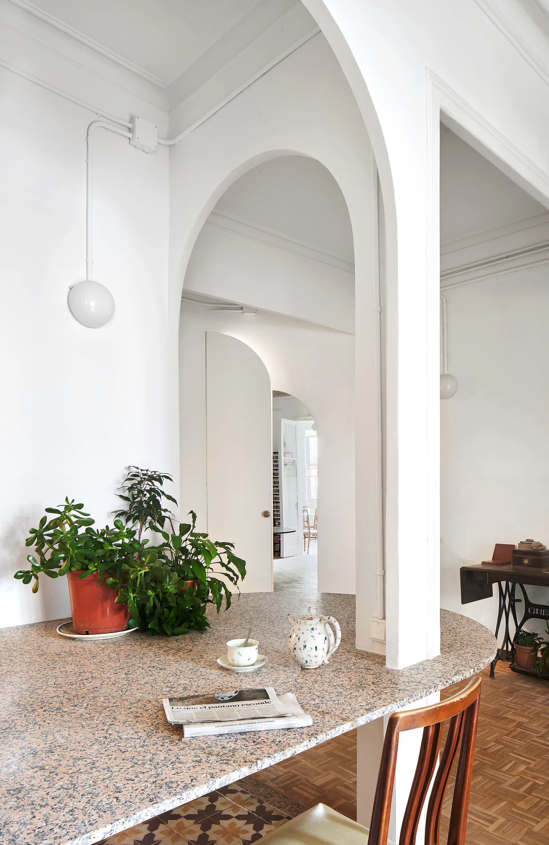 A dining room featuring a speckled table with a tea set and plant, framed by several prominent white arched openings.