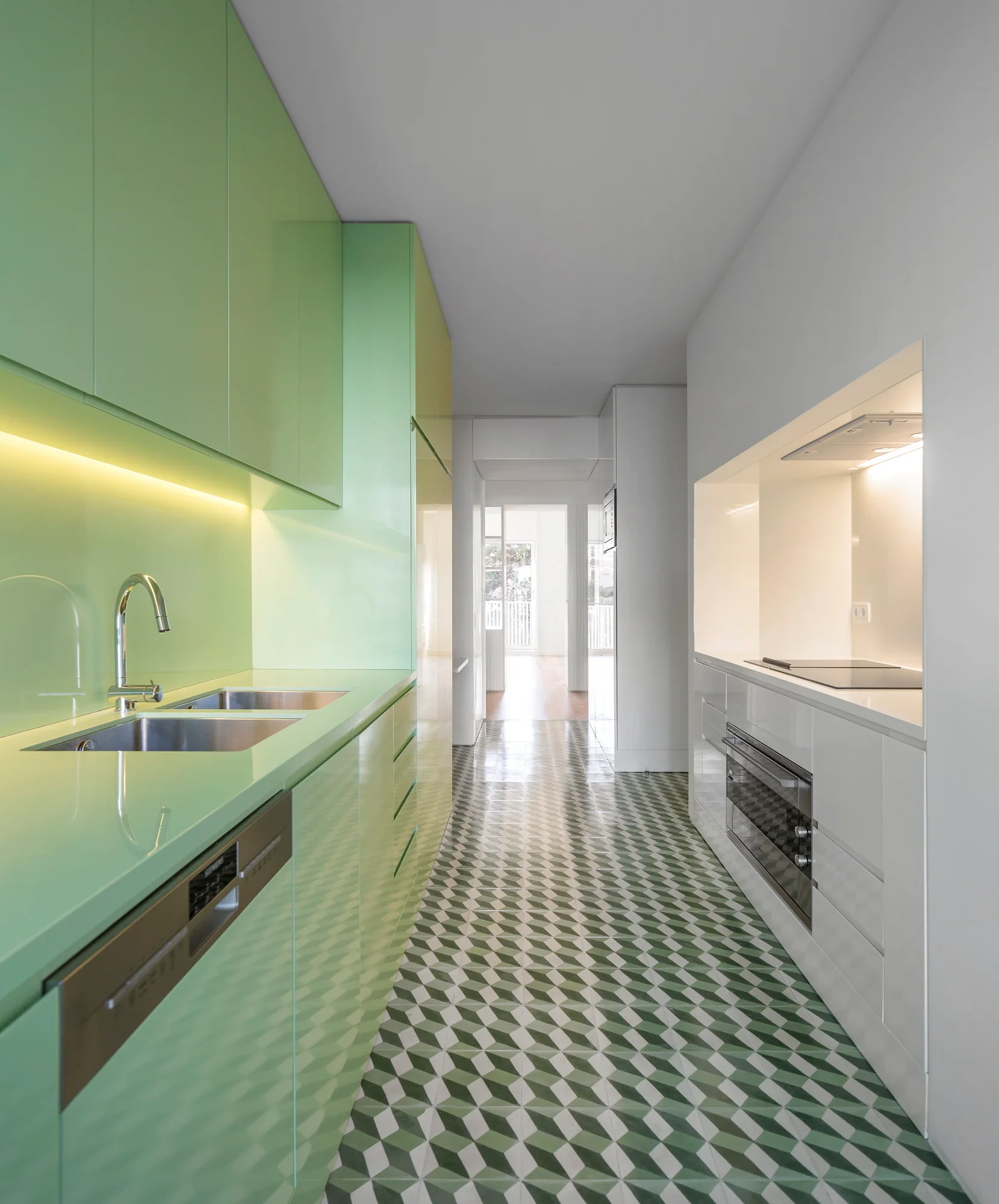 A galley kitchen with glossy green cabinets on one side, white cabinets on the other, and a geometric green and white tile floor.
