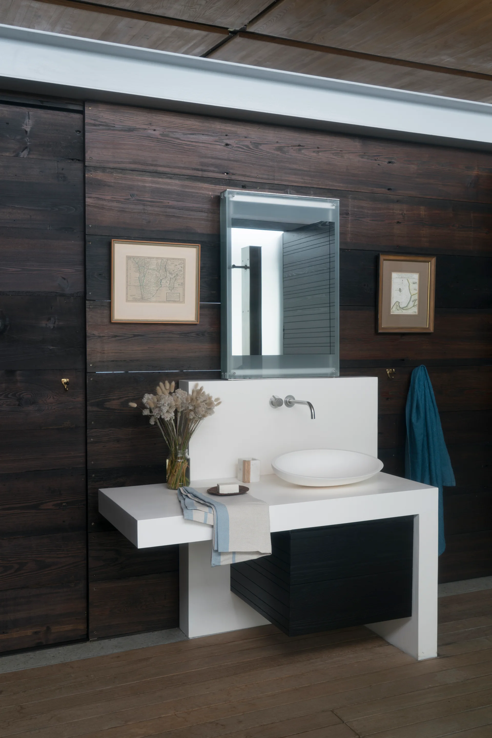 A modern bathroom features a white monolithic vanity with a vessel sink set against dark horizontal wood wall paneling.