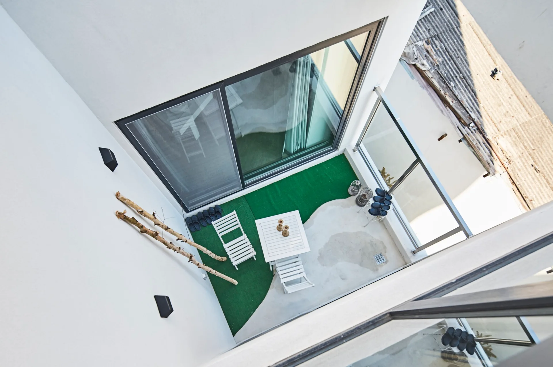 An overhead view of a small minimalist courtyard with a white bistro set on a split floor of green artificial turf and concrete.