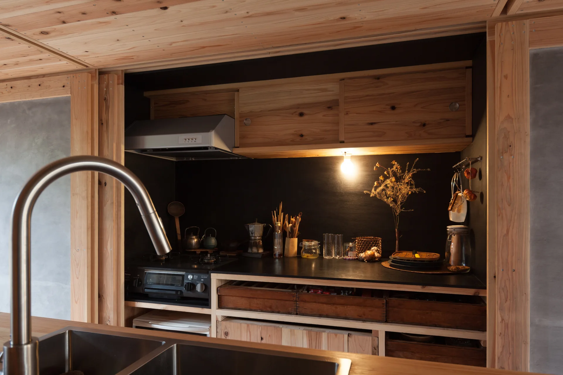 A rustic kitchen features a black countertop and backsplash accented by natural wood cabinetry, a stainless steel faucet, and a gas stovetop.