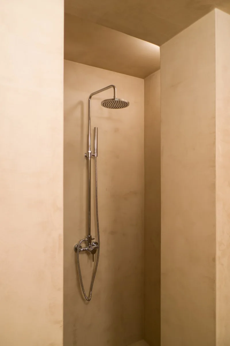 A chrome rainfall showerhead and handheld wand installed inside a recessed shower niche with smooth, warm beige plaster walls.