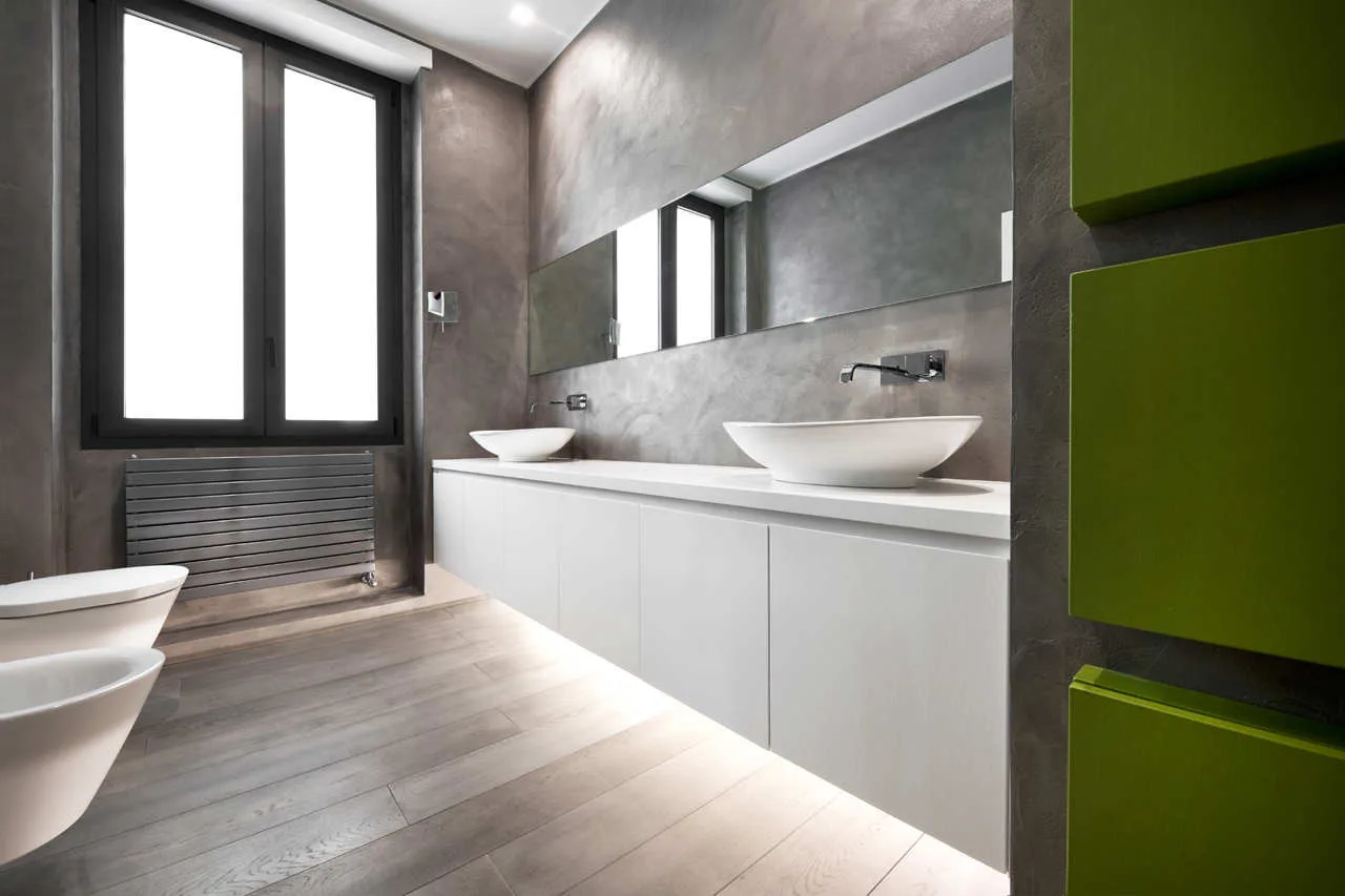 A minimalist bathroom features a long white floating vanity with double vessel sinks against textured gray plaster walls and wood-look flooring.
