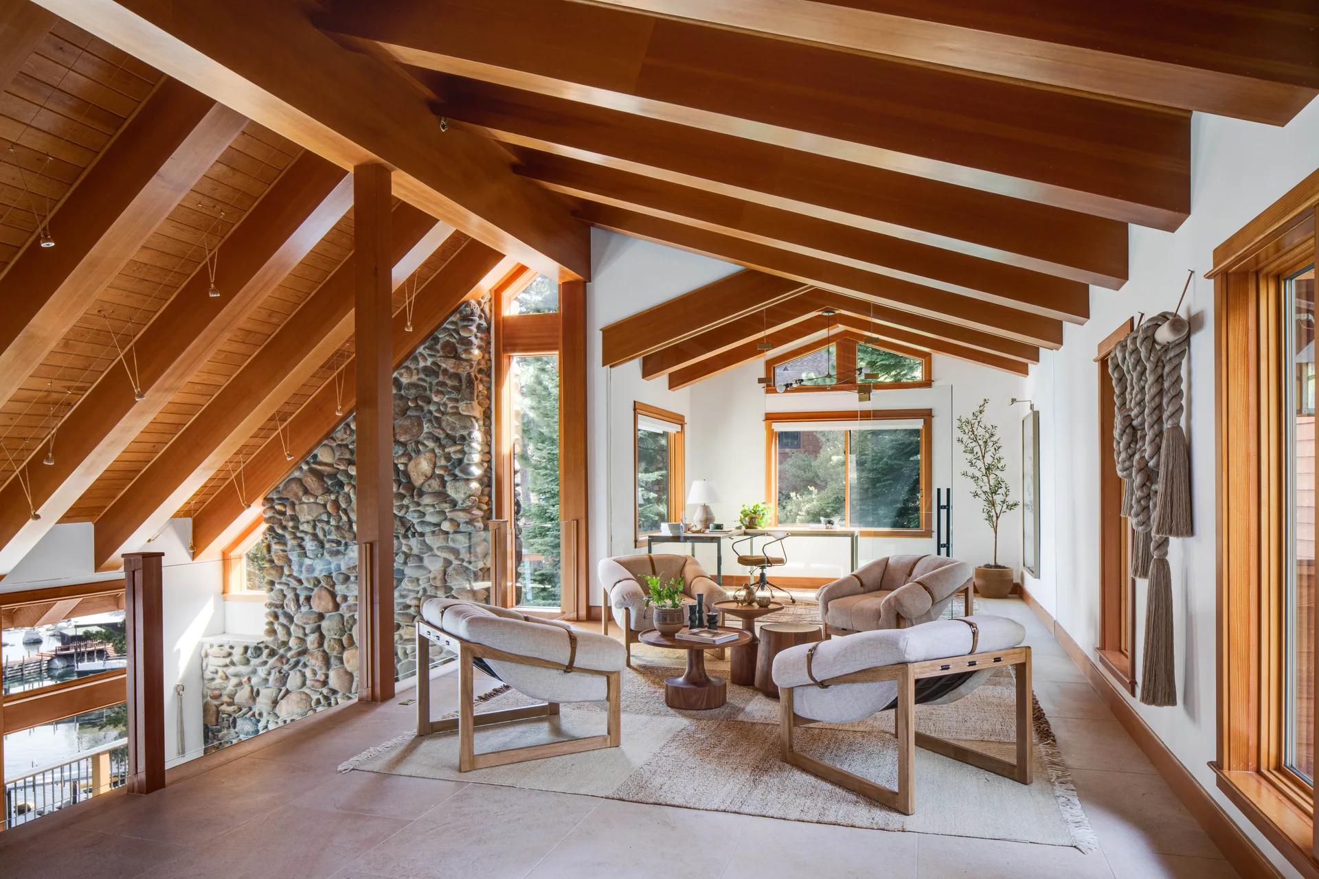 A lofted living space with a vaulted wood beam ceiling, natural stone accent wall, and four upholstered armchairs gathered around a central table.