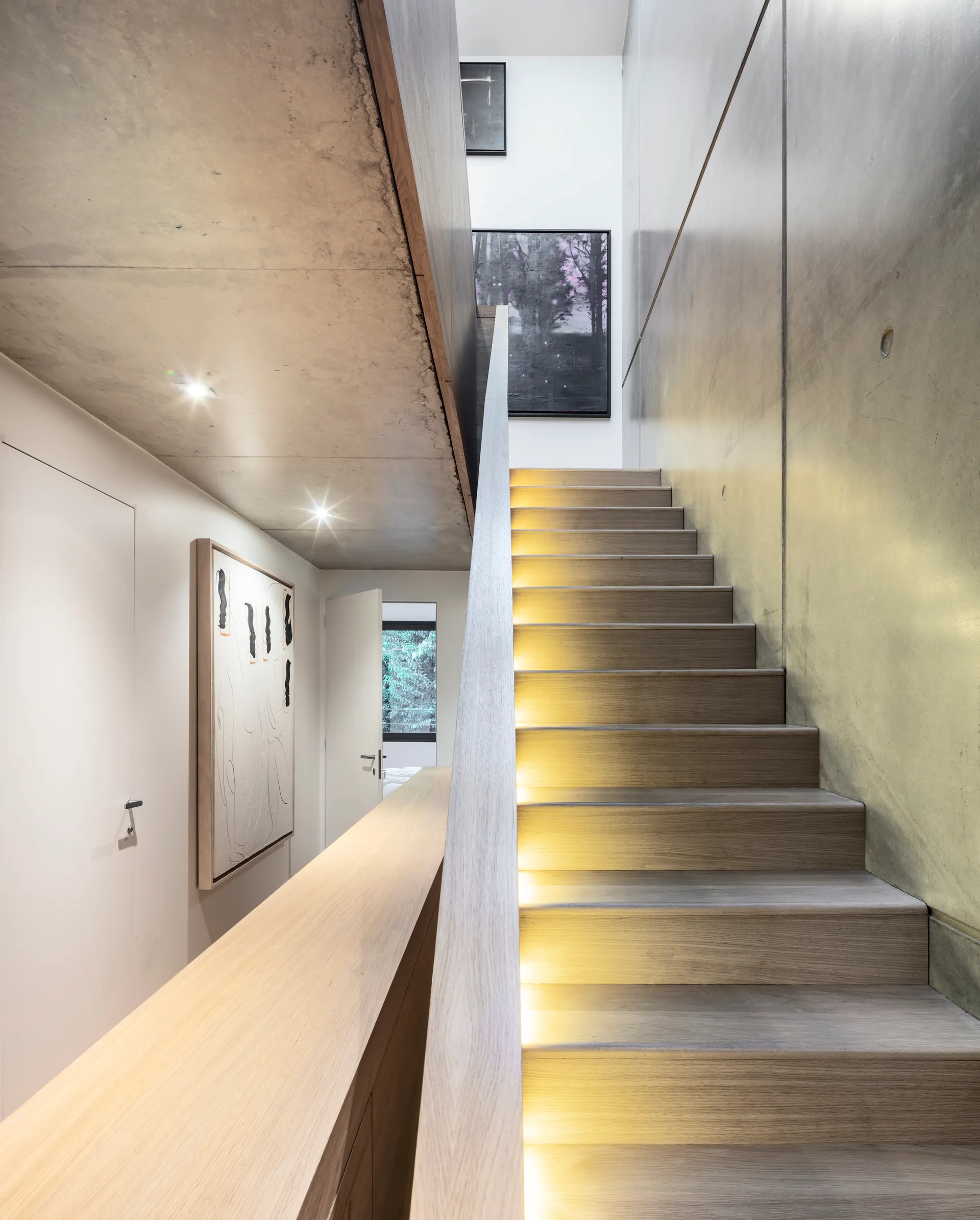 A modern wooden staircase with illuminated steps runs alongside a smooth concrete wall.