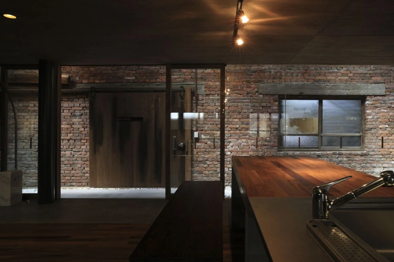 An industrial loft kitchen features a dark wood island with a metal faucet set against a red brick wall with a sliding barn door.