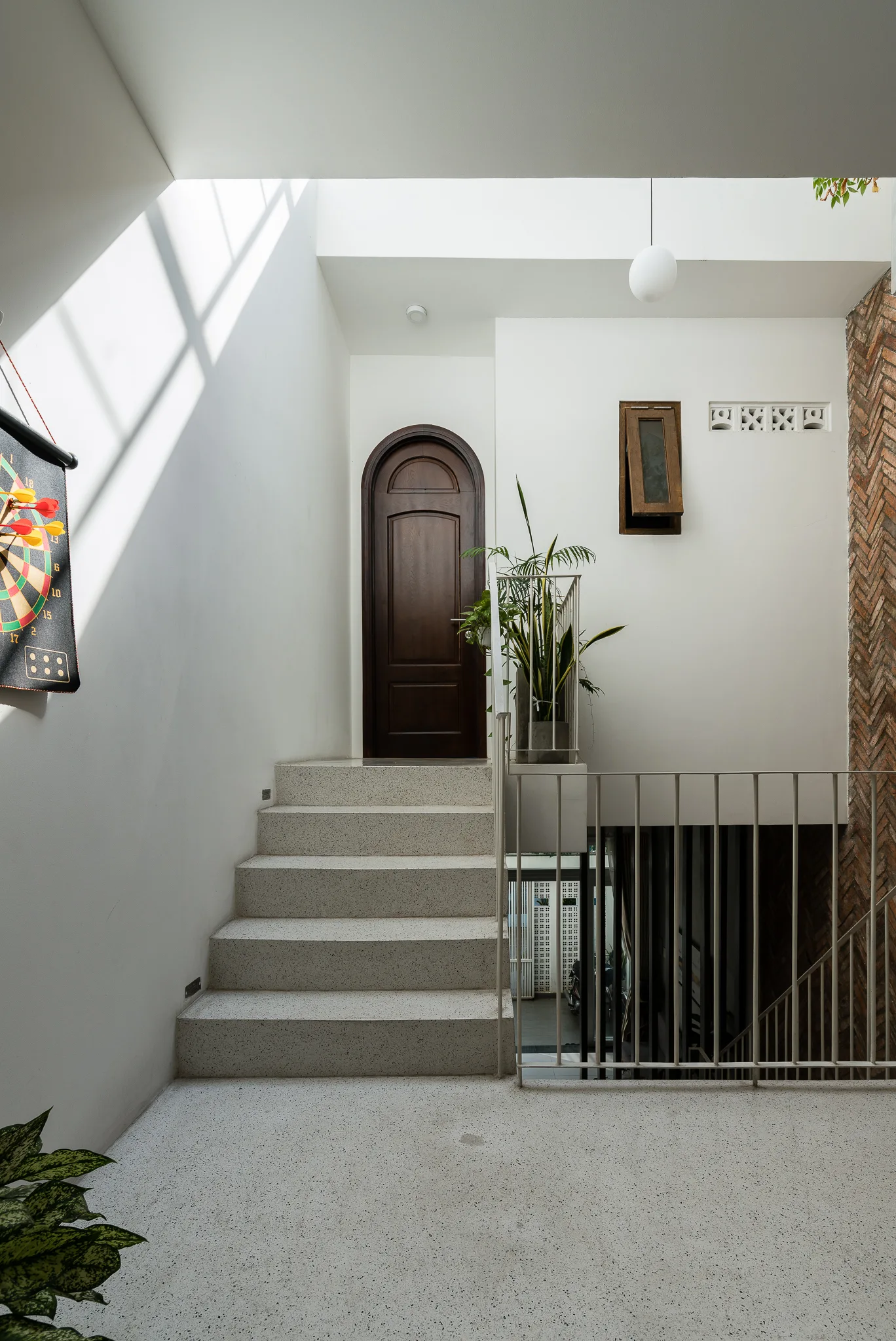 A modern staircase with speckled terrazzo steps leads up to an arched dark wood door next to a herringbone patterned brick accent wall.