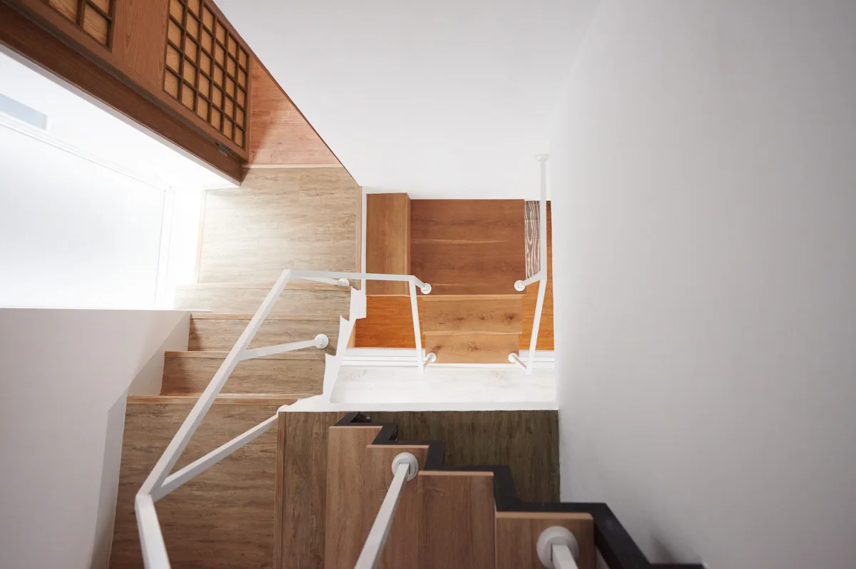 An overhead look down a multi-level wooden staircase with clean white geometric railings and smooth white walls.