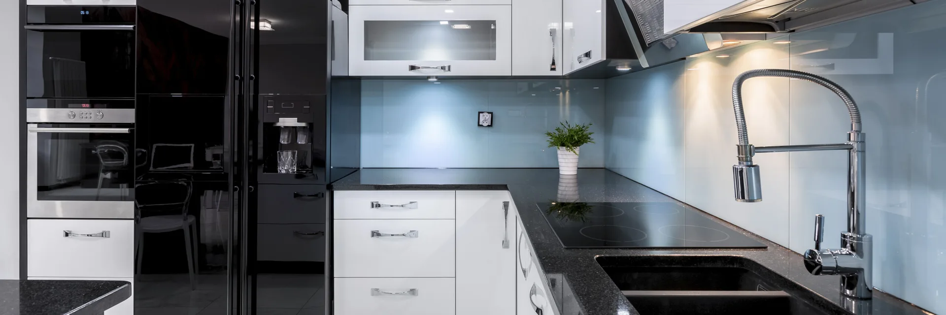 A contemporary kitchen features glossy white cabinetry, black granite countertops, a light blue glass backsplash, and a modern chrome pull-down faucet.