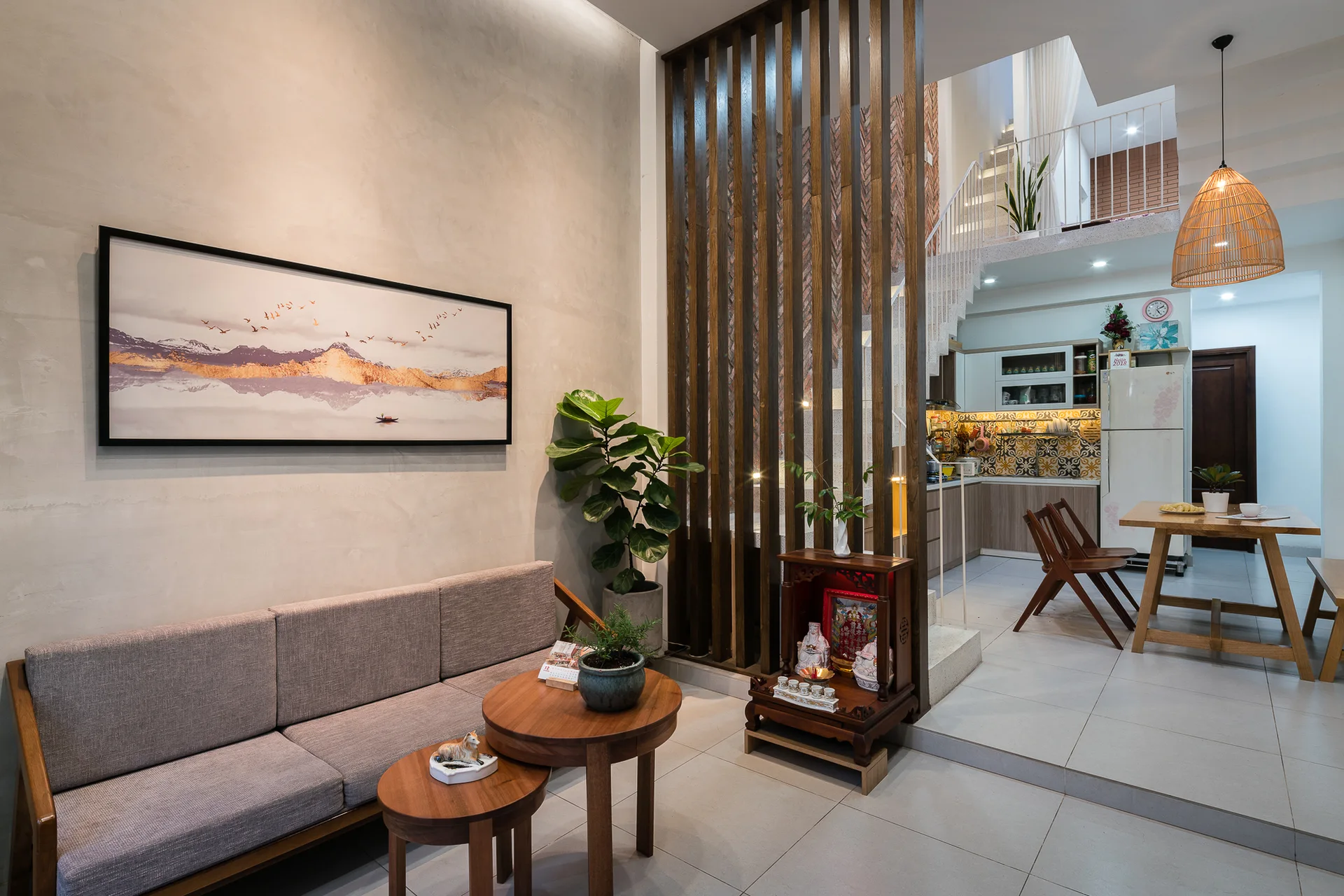 An open-plan living room features a grey sofa, round nesting coffee tables, a wooden vertical slat screen, and a kitchen in the background.