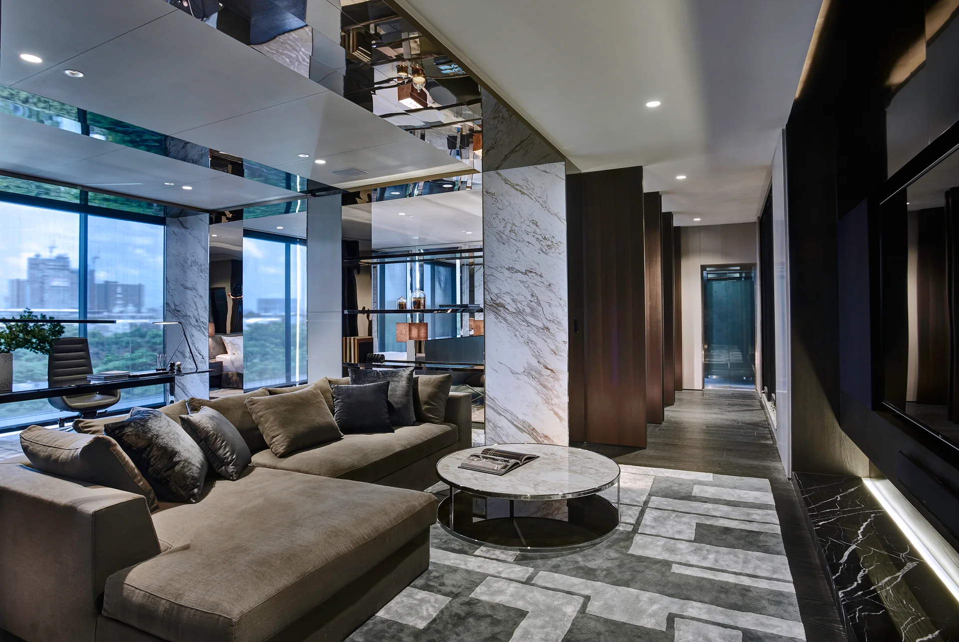 A modern living room features a brown sectional sofa, a marble coffee table, a geometric rug, and reflective mirrored ceiling panels.