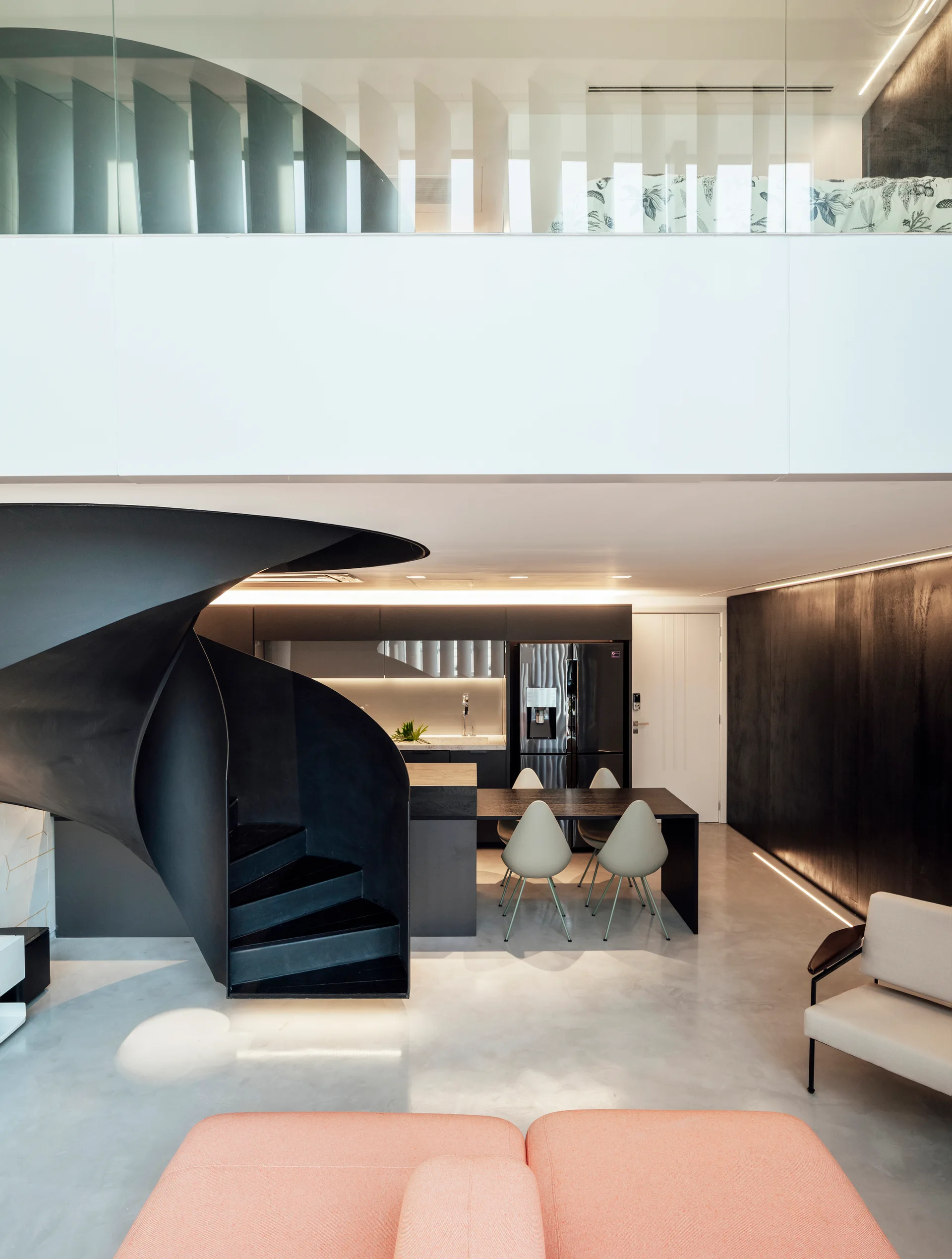 A modern open-concept loft features a sculptural black spiral staircase, dark kitchen cabinets, concrete-style flooring, and a peach sofa.